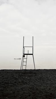 A stark lifeguard stand on a deserted beach with calm ocean backdrop.