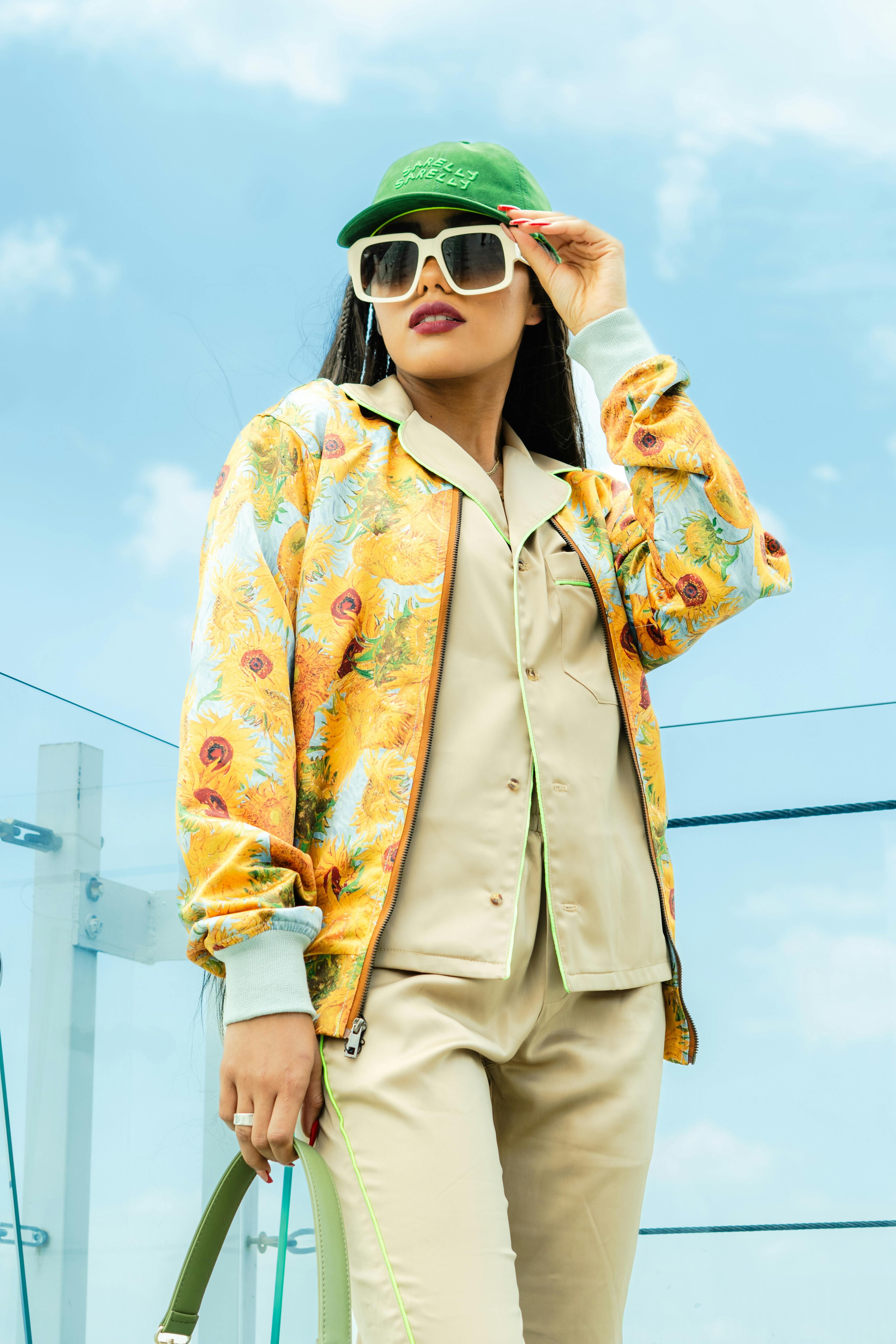 Free Woman in colorful jacket and green cap posing outdoors with blue sky backdrop. Stock Photo