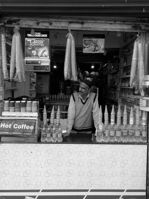 Free Monochrome image of a street vendor at a small stall, selling snacks and hot coffee. Stock Photo