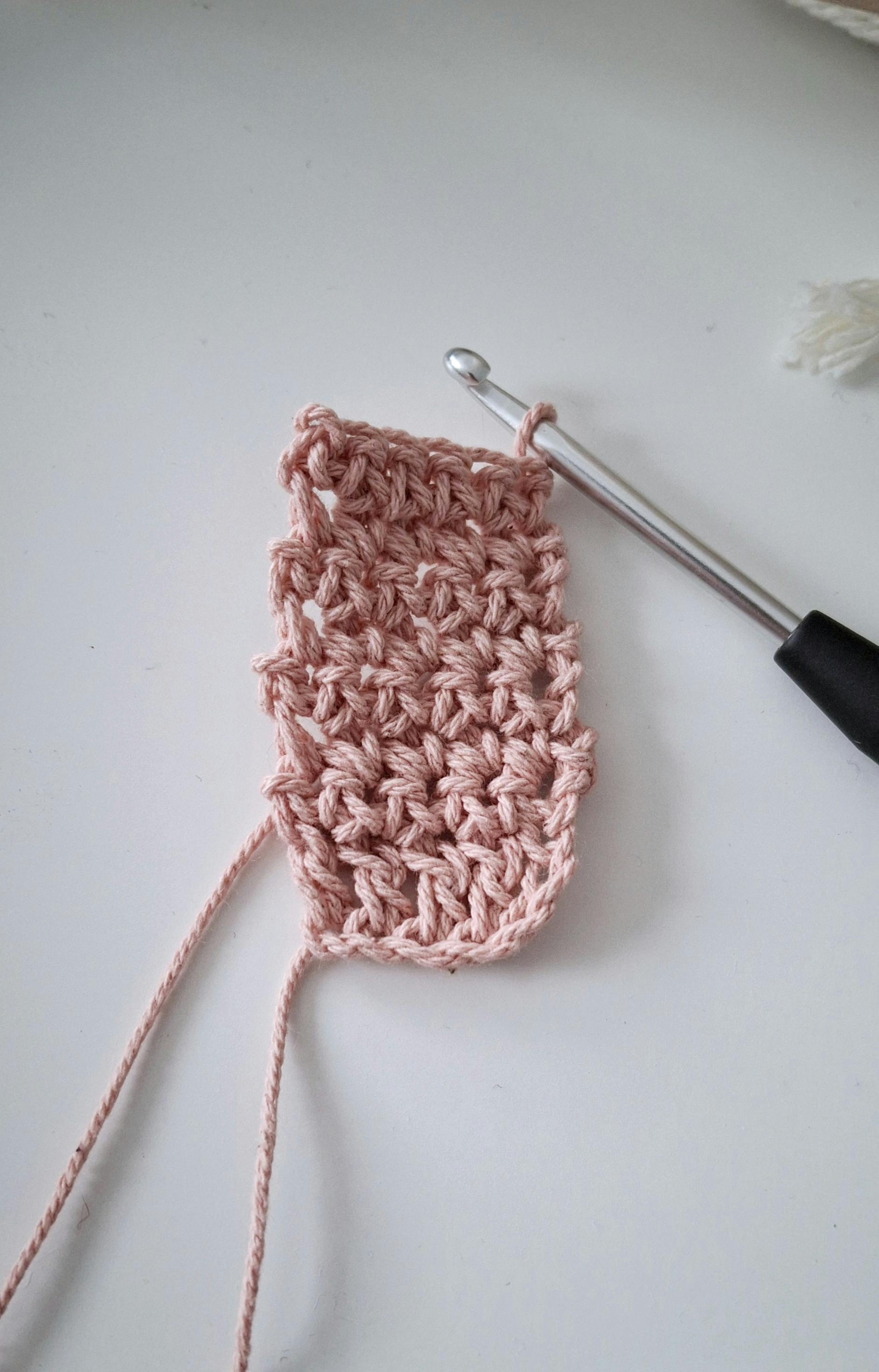 A close-up of a handcrafted crocheted piece in progress with a crochet hook on a white surface.