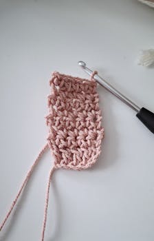 A close-up of a handcrafted crocheted piece in progress with a crochet hook on a white surface.