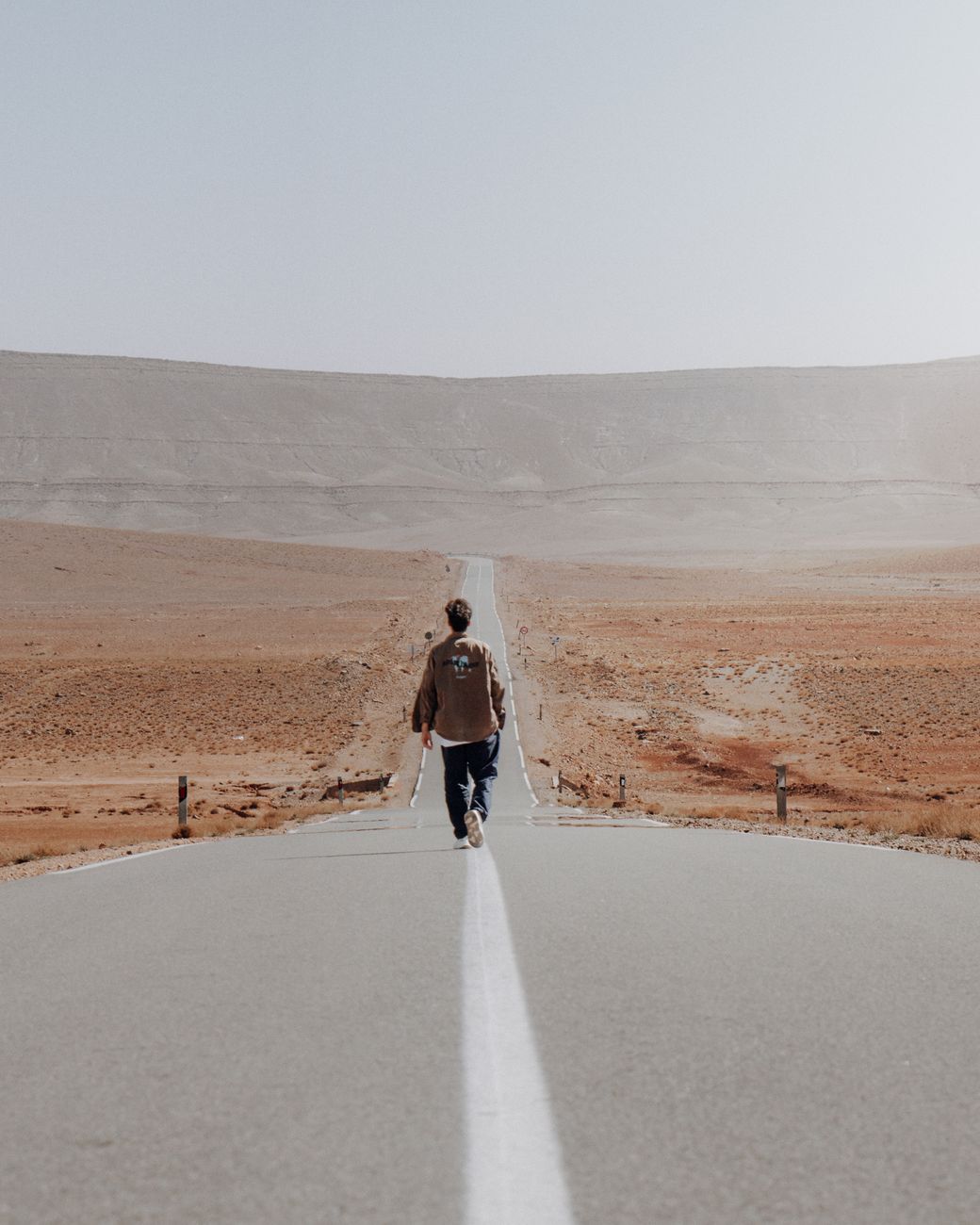 A lone traveler walking along an empty desert road through the Moroccan landscape.