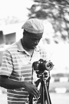 Black and white image of a young male photographer setting up a Canon camera outdoors on a tripod.