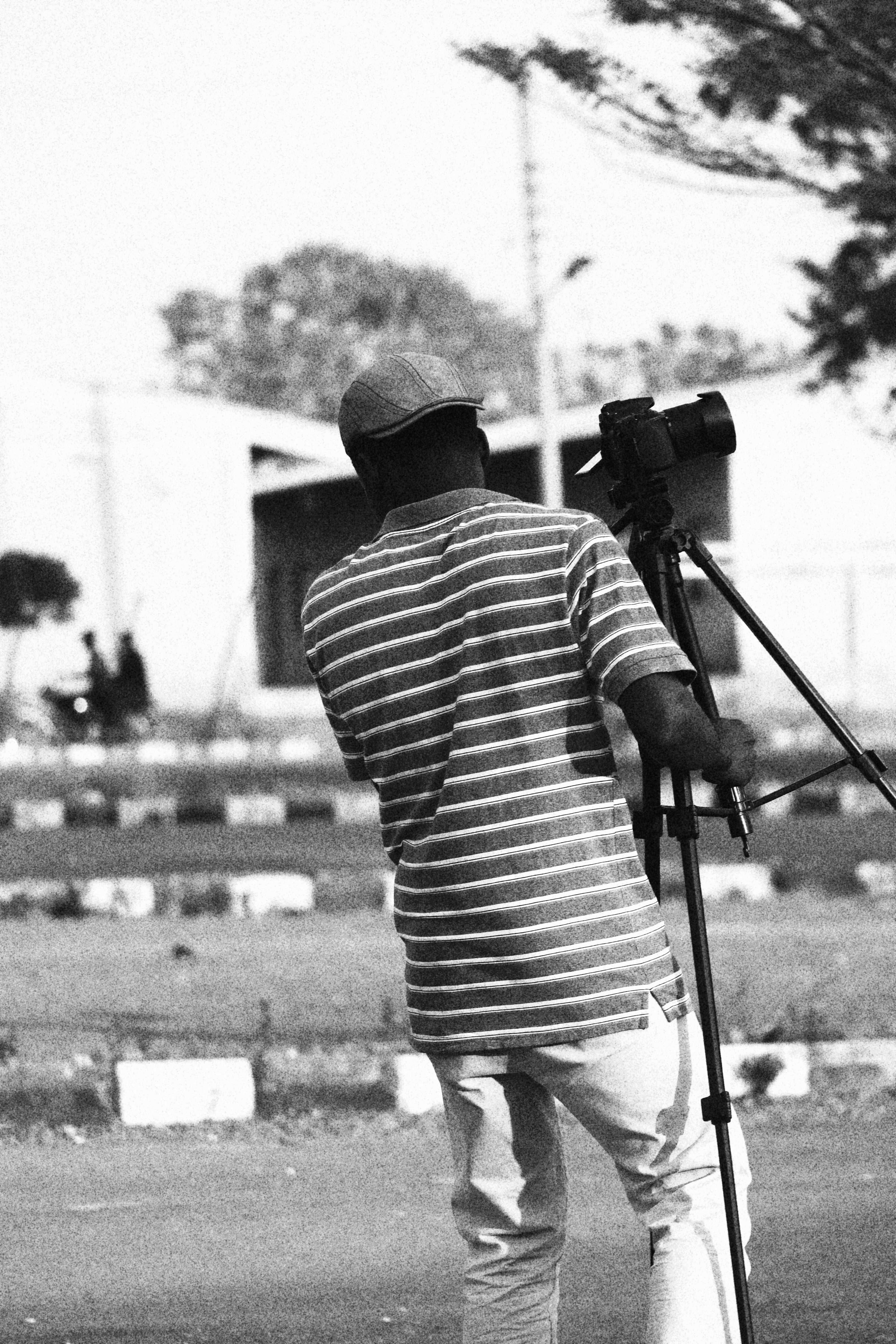 Black and white image of a photographer with a camera tripod in a park setting.