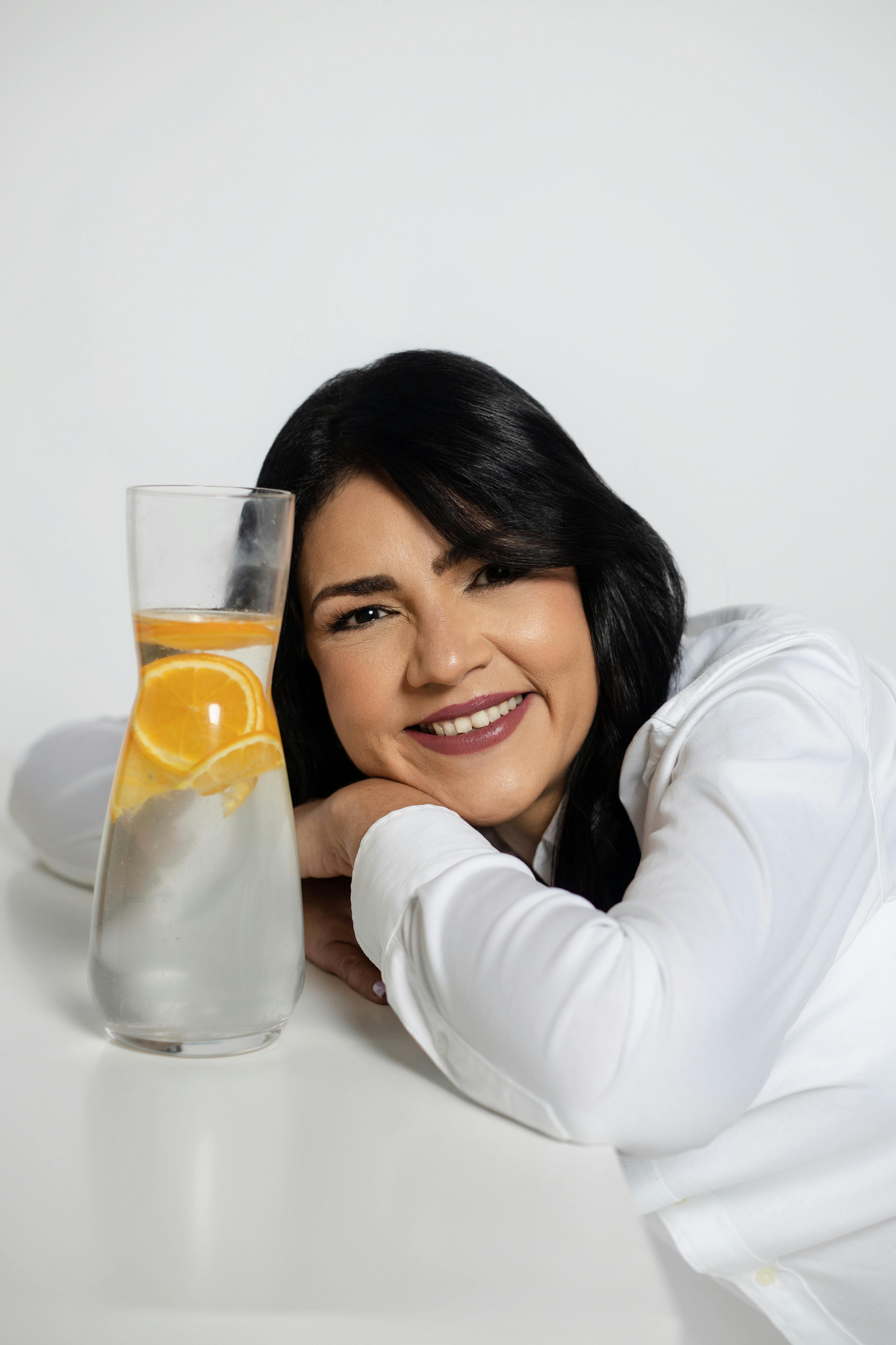 Relaxed woman smiling next to a glass of refreshing citrus-infused water.