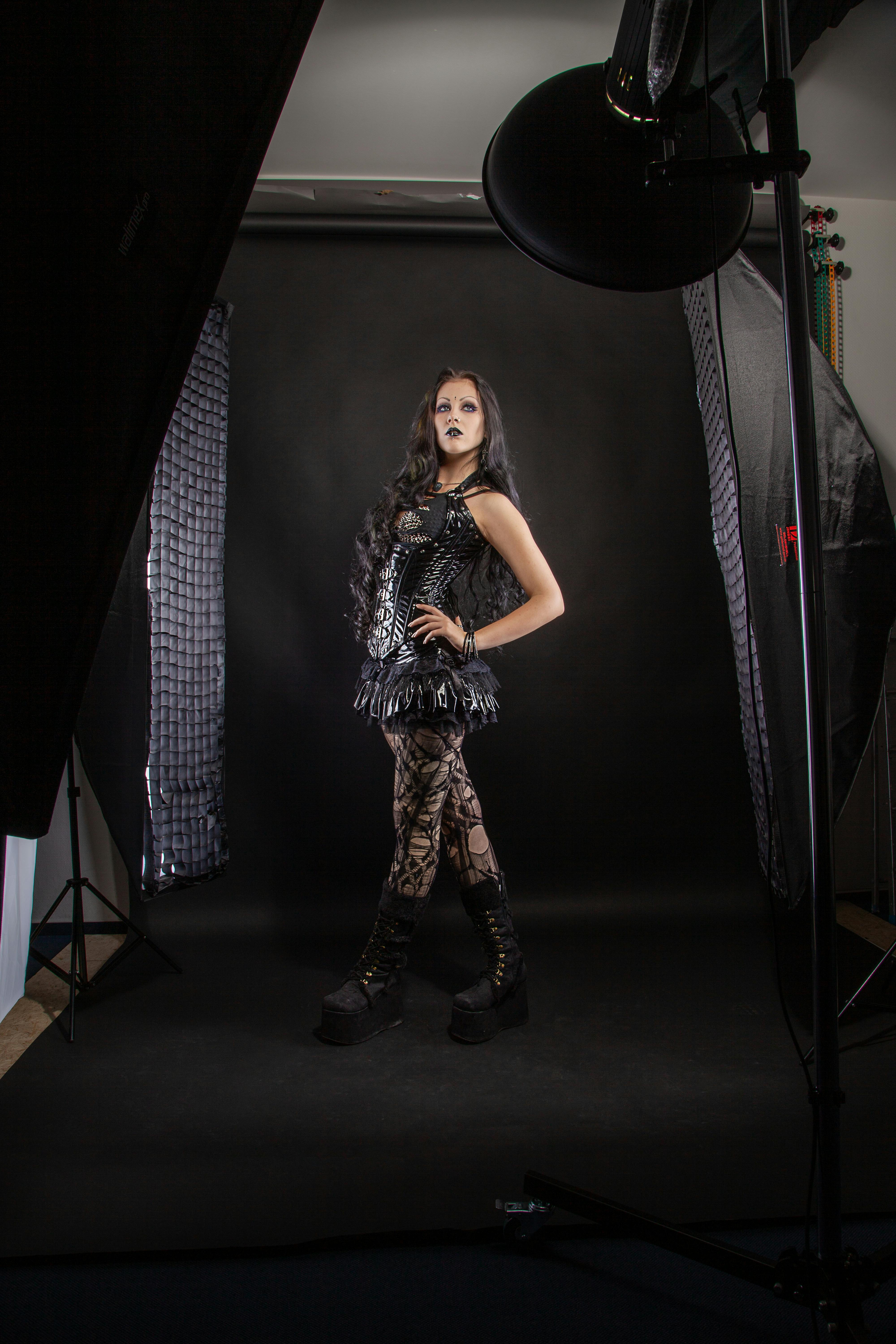 Dark-themed gothic fashion portrait of a young woman in a studio setting.