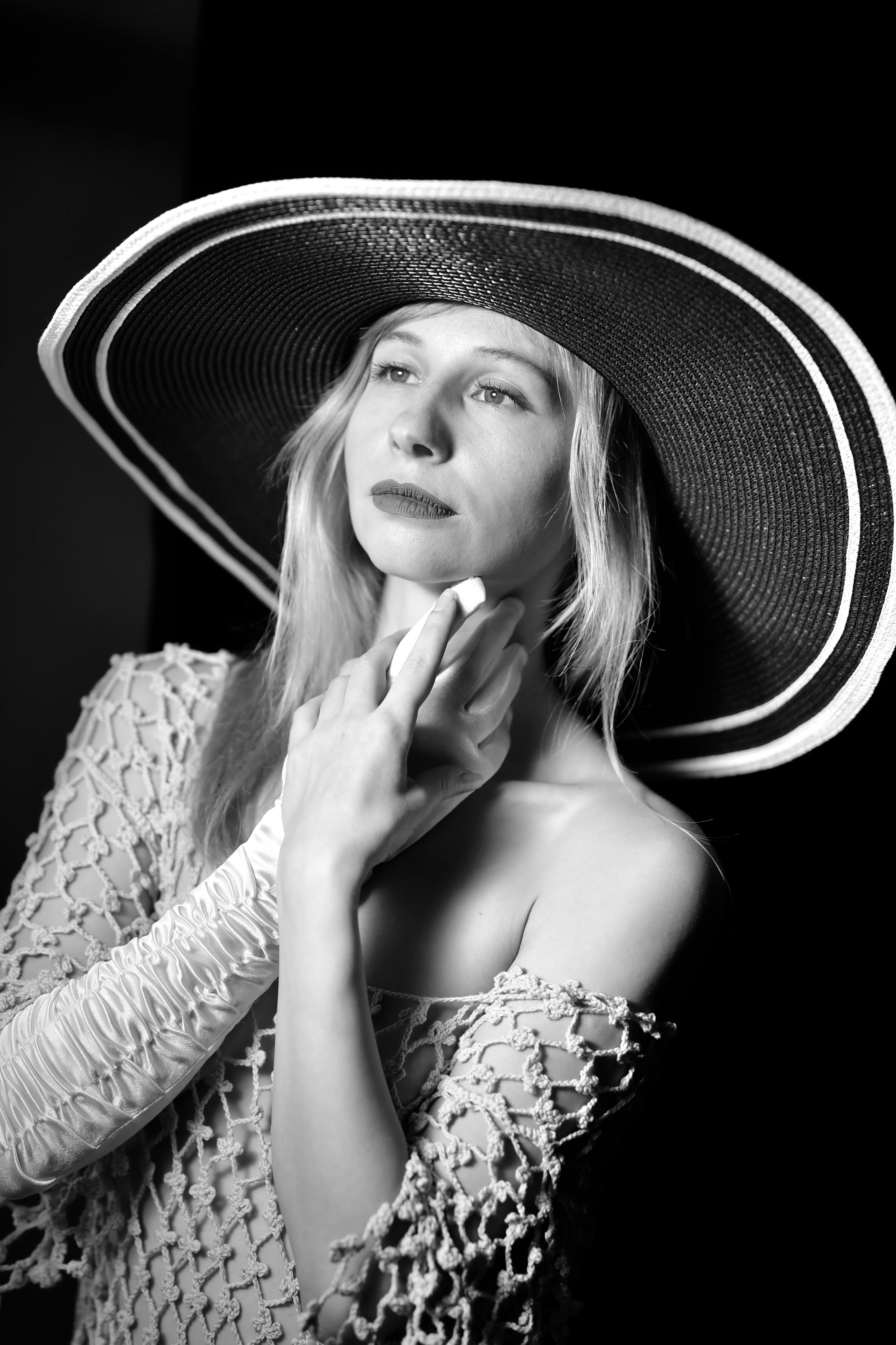 这幅时尚的黑白肖像描绘了一位戴着宽边帽的女性，背景是工作室环境