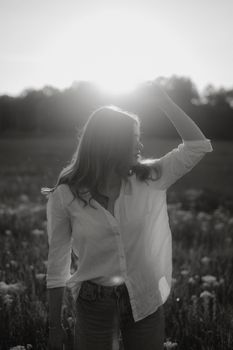 Black and white portrait of a woman in a field backlit by the setting sun.