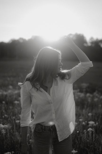 Black and white portrait of a woman in a field backlit by the setting sun.