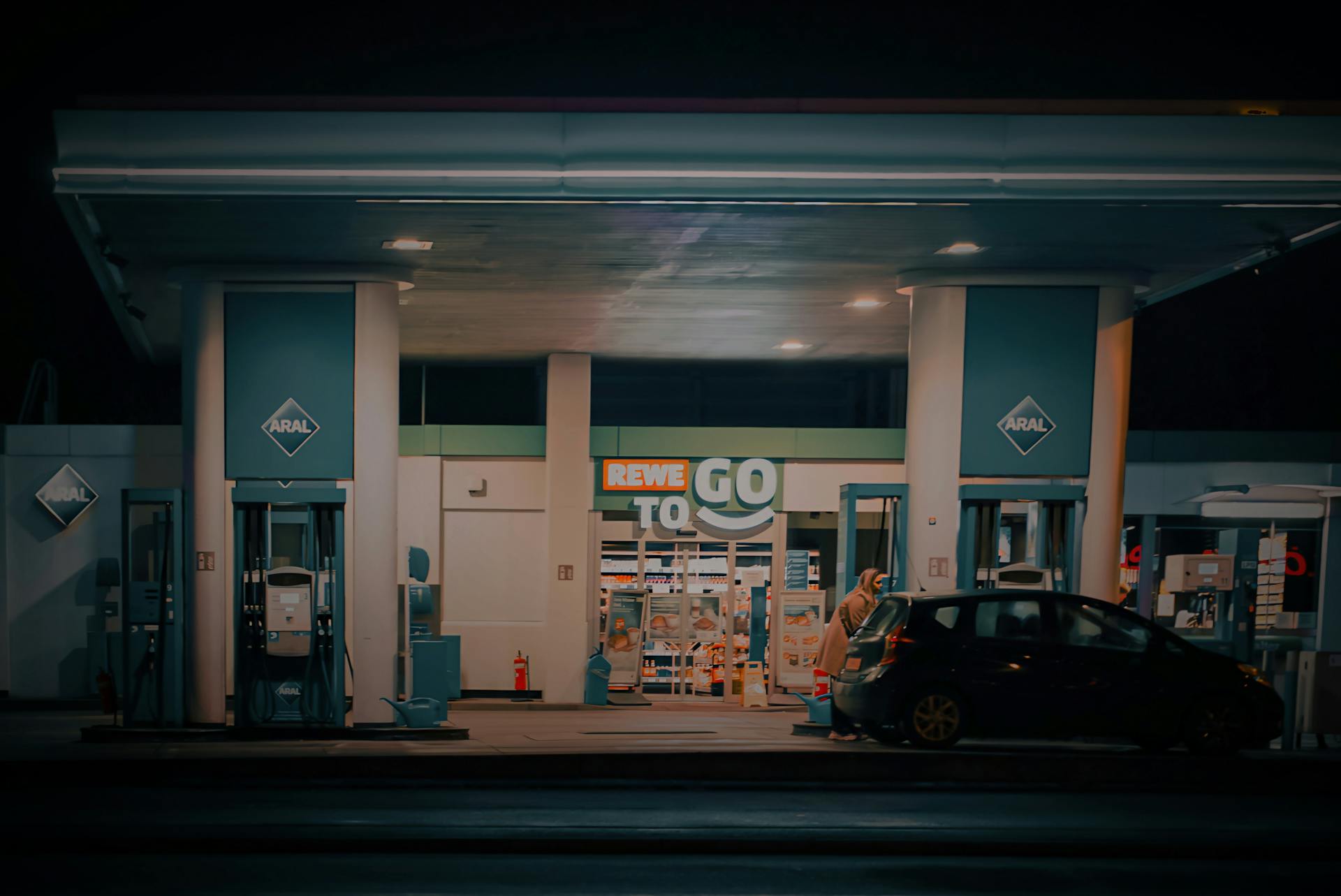 A nighttime view of a gas station and convenience store with a car parked at the pump.