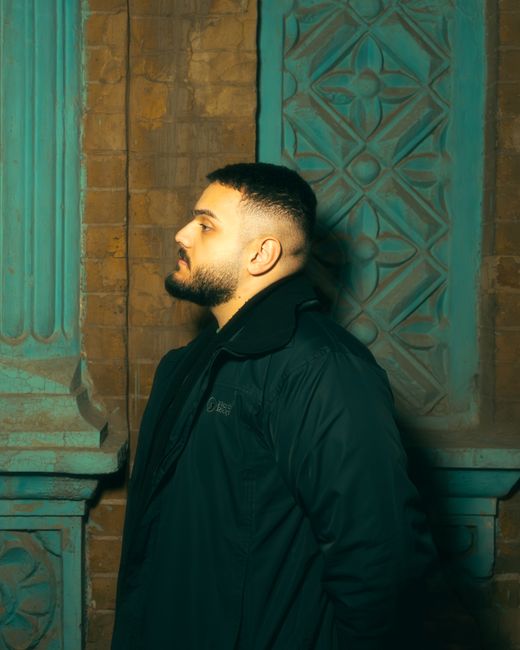 Side view of a man with a beard standing against a decorated brick wall.