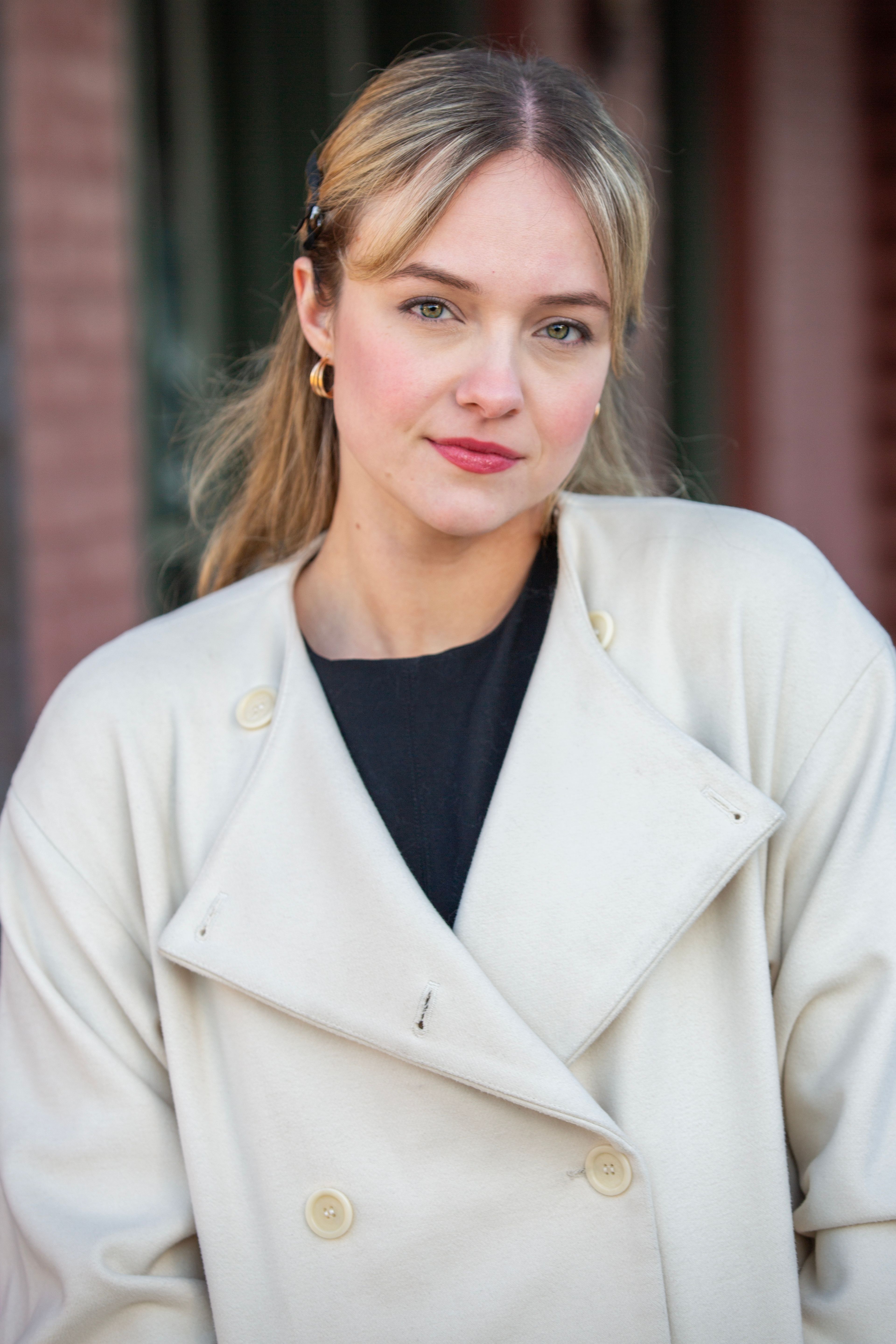 Charming woman in a stylish white coat poses outdoors, exuding elegance and confidence.