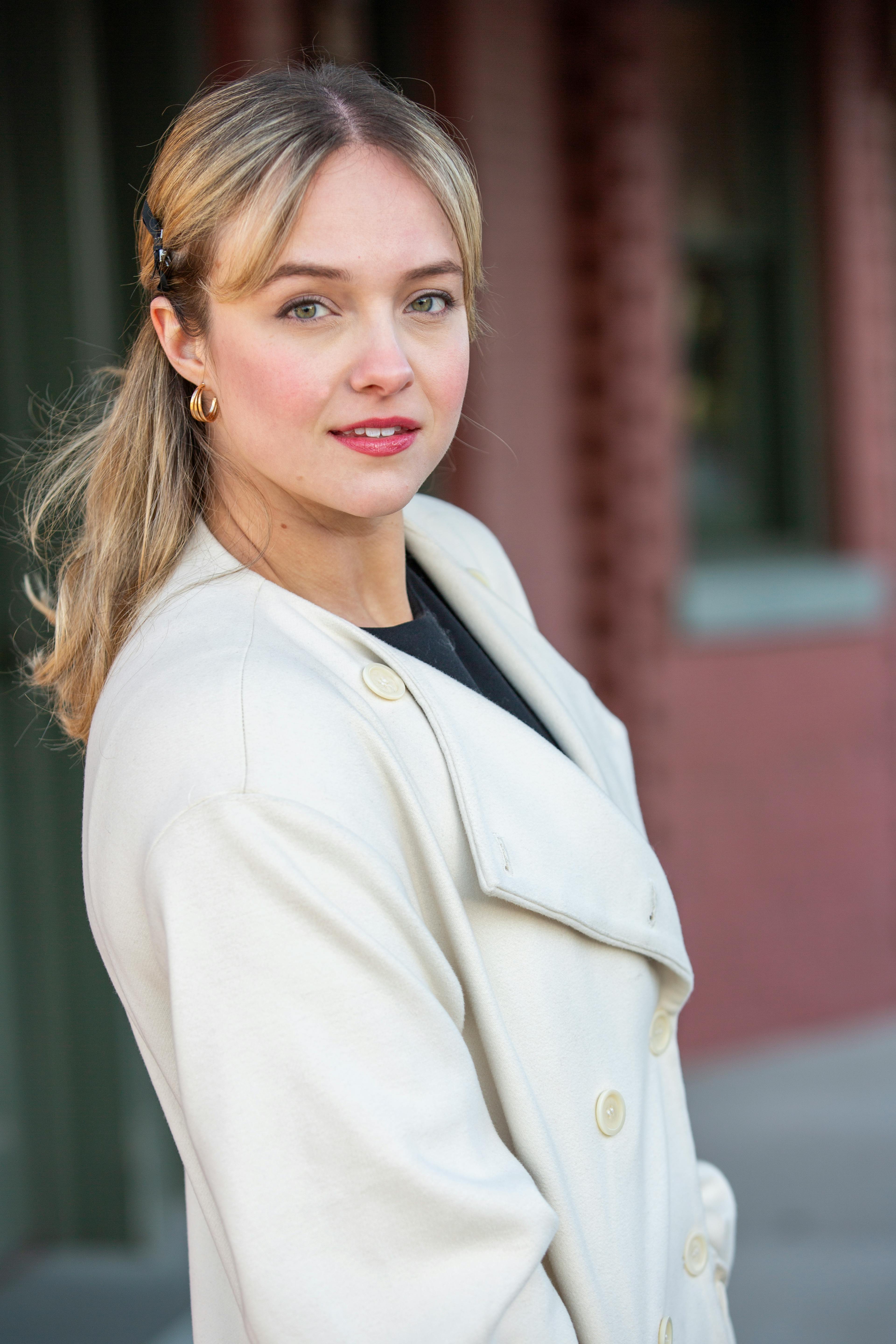 Portrait of a woman in a white coat in an urban setting, showcasing elegance and style.