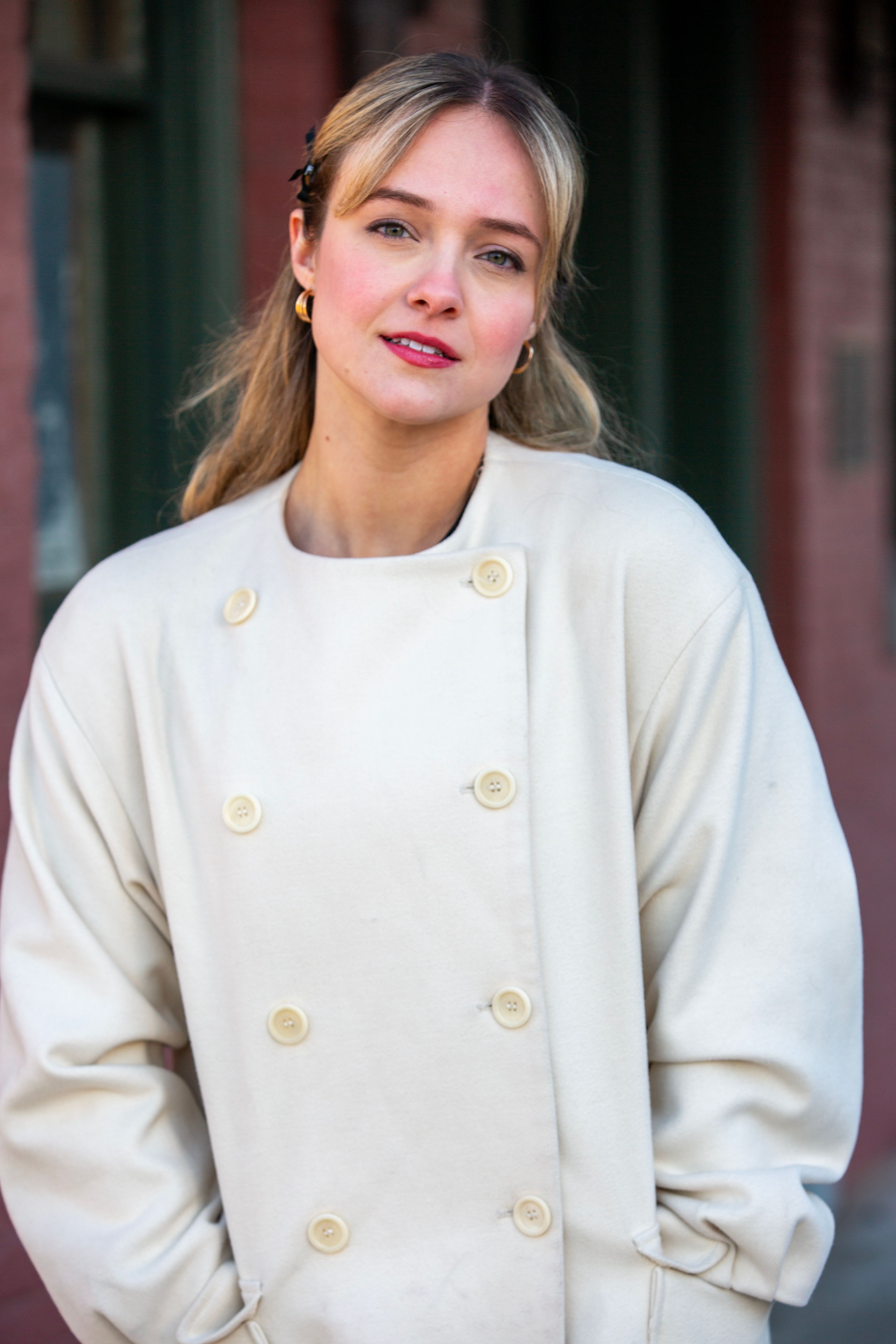 Elegant woman outdoors wearing a stylish white coat with bright red lipstick.