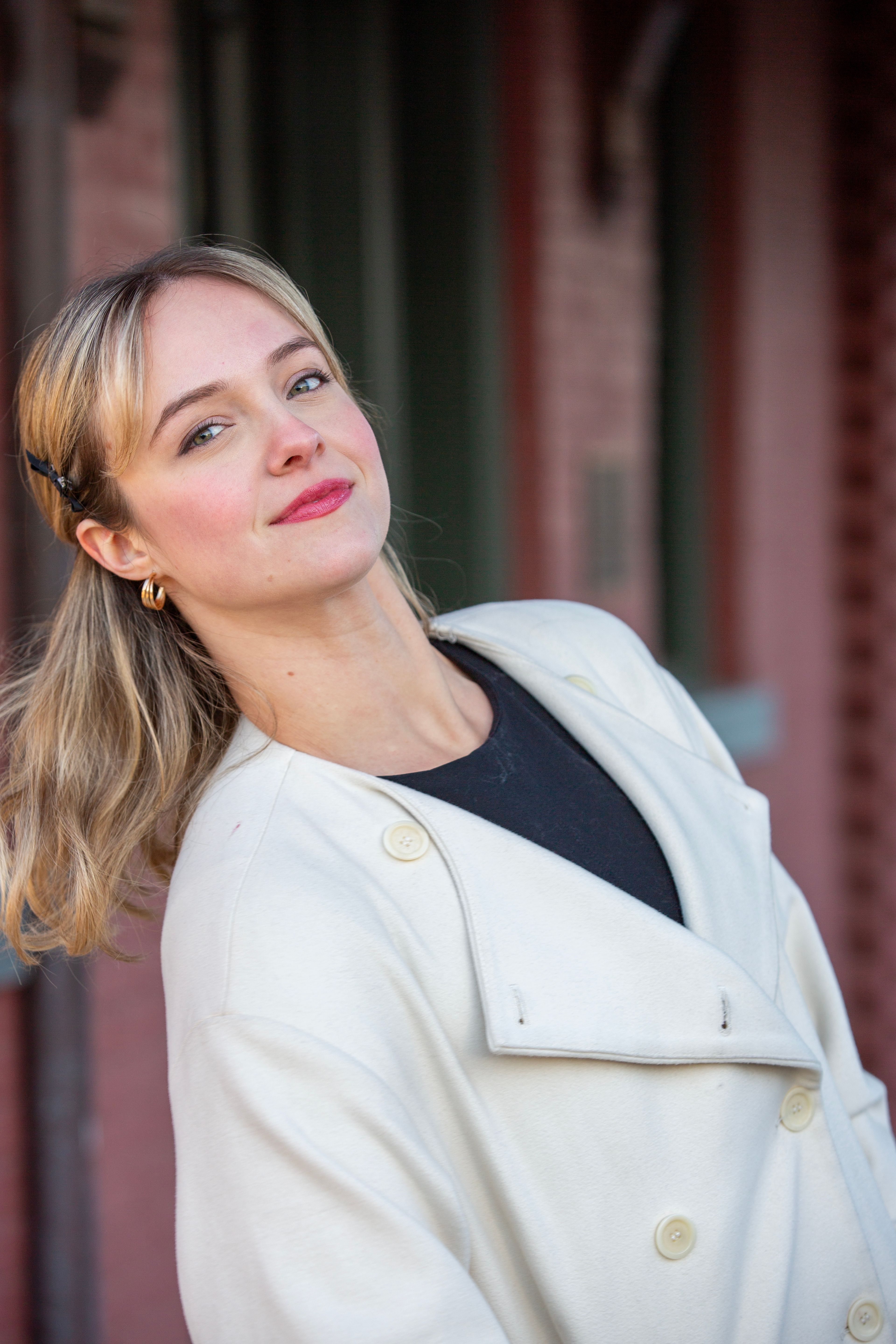 Portrait of a smiling woman in a white coat against an urban background.