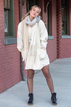 Fashionable woman in winter attire posing against brick wall outdoors.