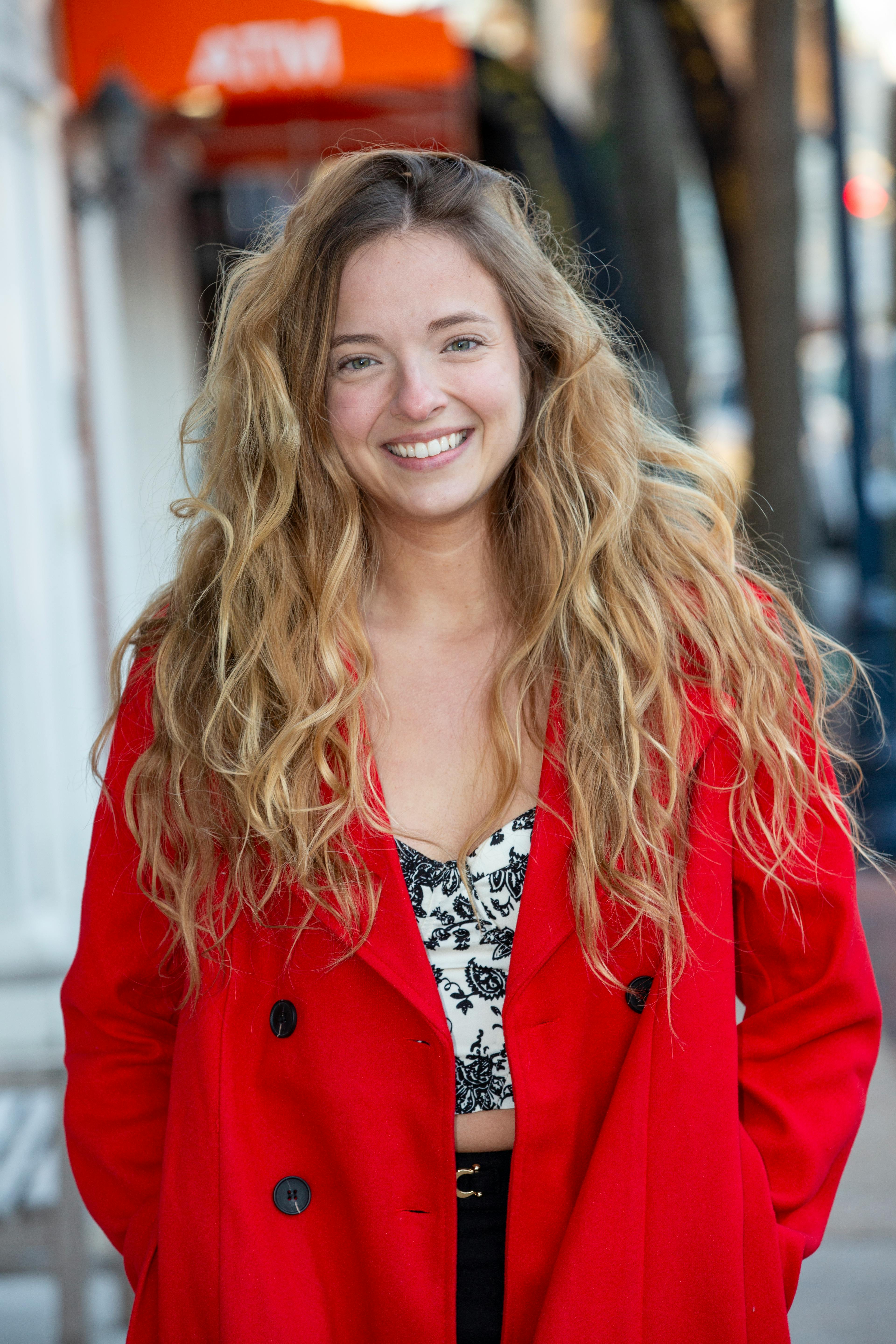 Cheerful woman in vibrant red coat, smiling on a city street.