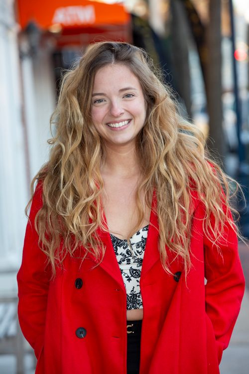 Free Cheerful woman in vibrant red coat, smiling on a city street. Stock Photo