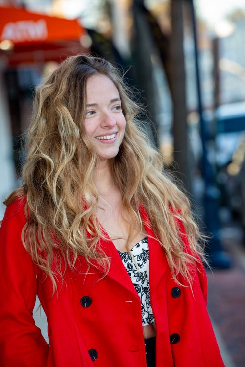 Free A happy woman with long hair smiles while wearing a red coat outdoors. Stock Photo