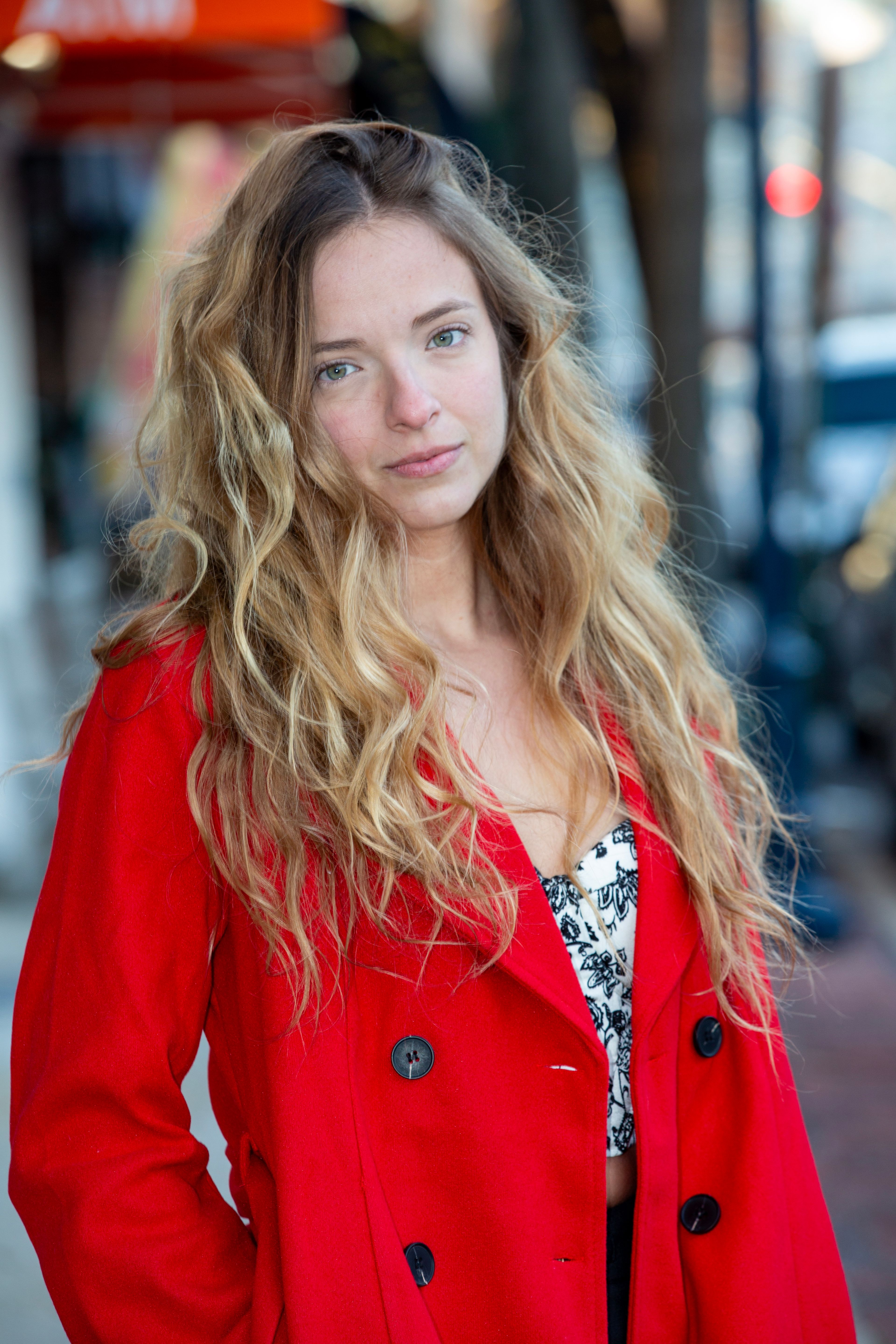 Portrait of a woman in a red coat, standing on a city sidewalk. Vibrant and contemporary.