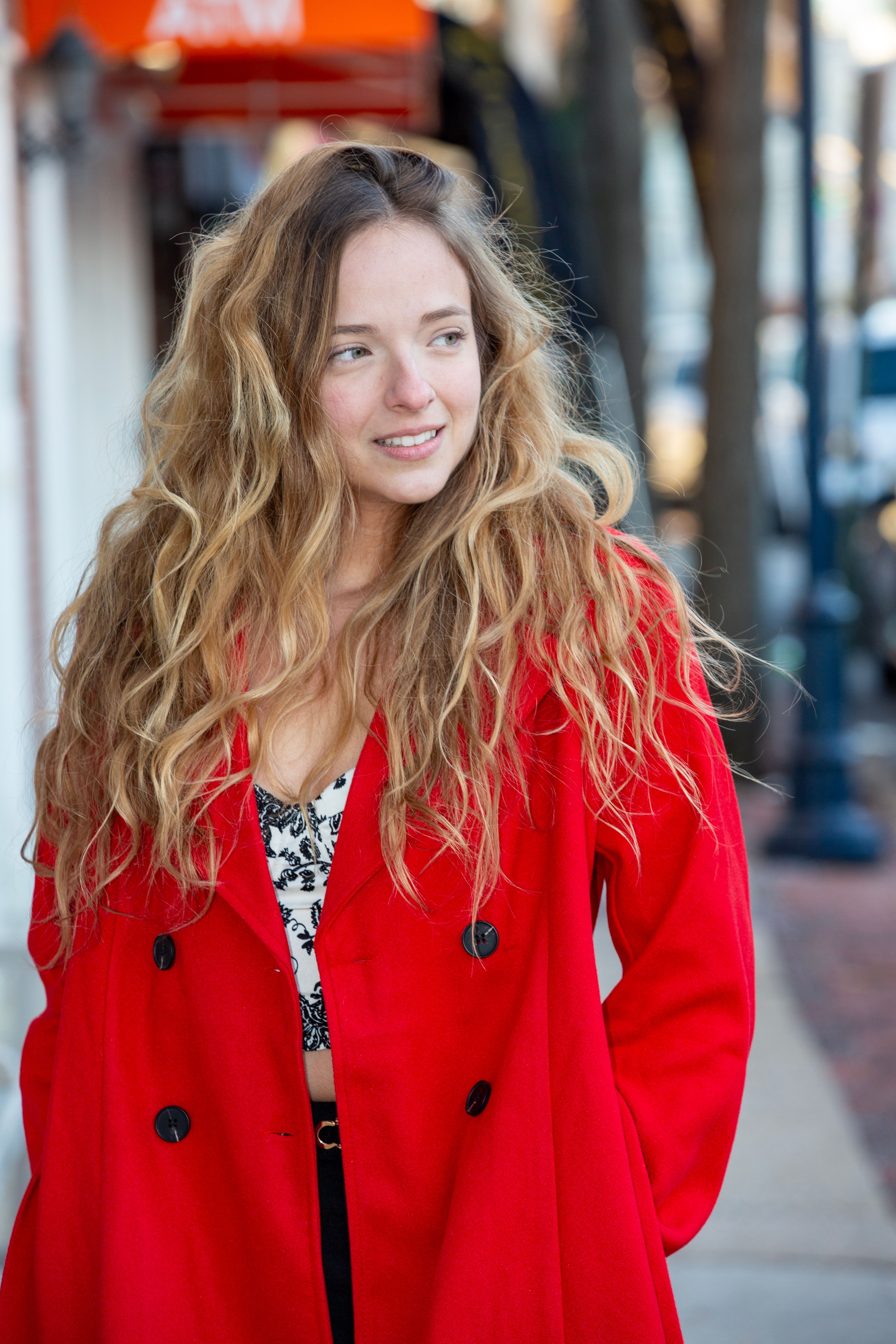 A young woman in a vibrant red coat walks confidently down a bustling city street.