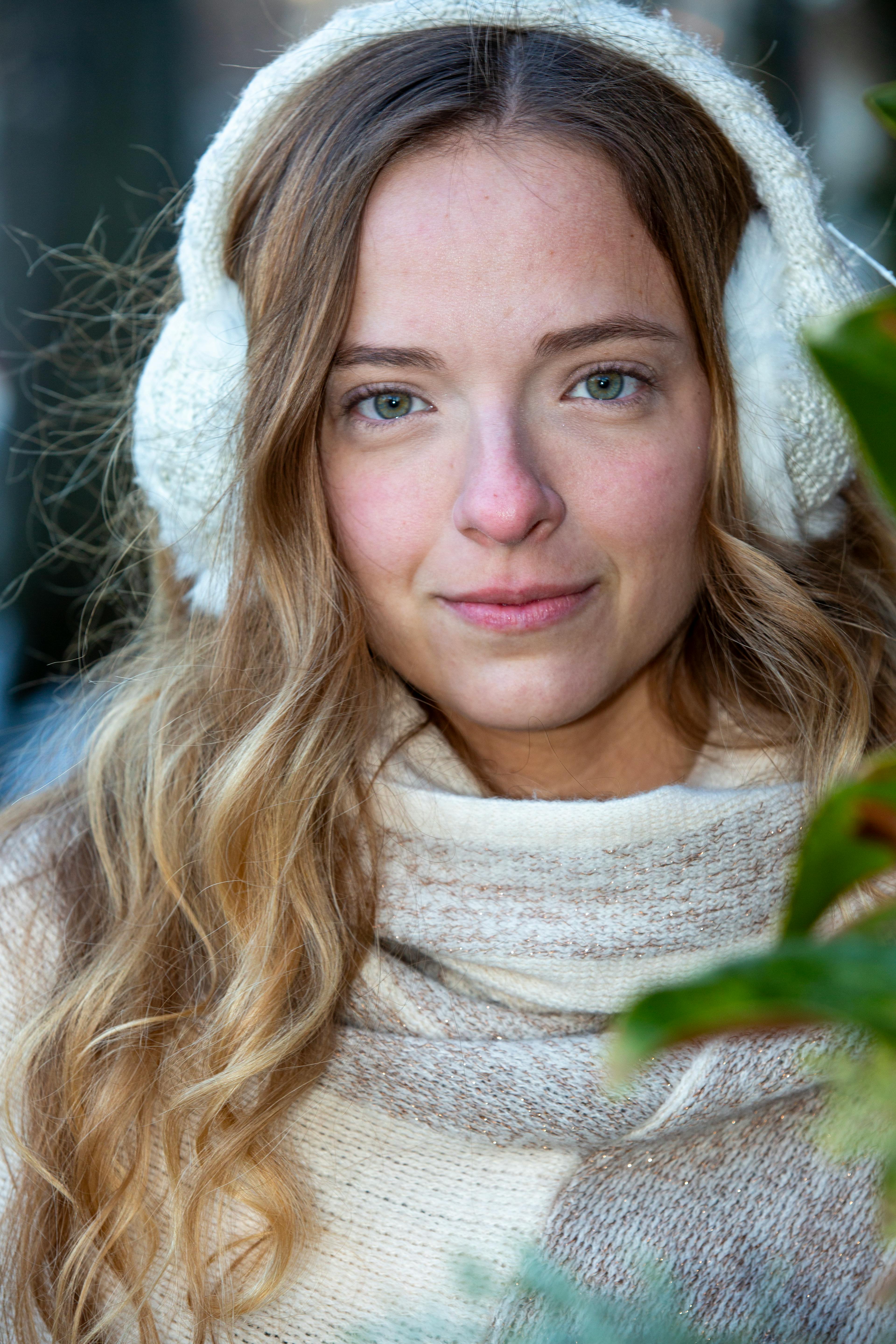 A close-up outdoor portrait of a woman with blonde hair wearing earmuffs in a winter setting.