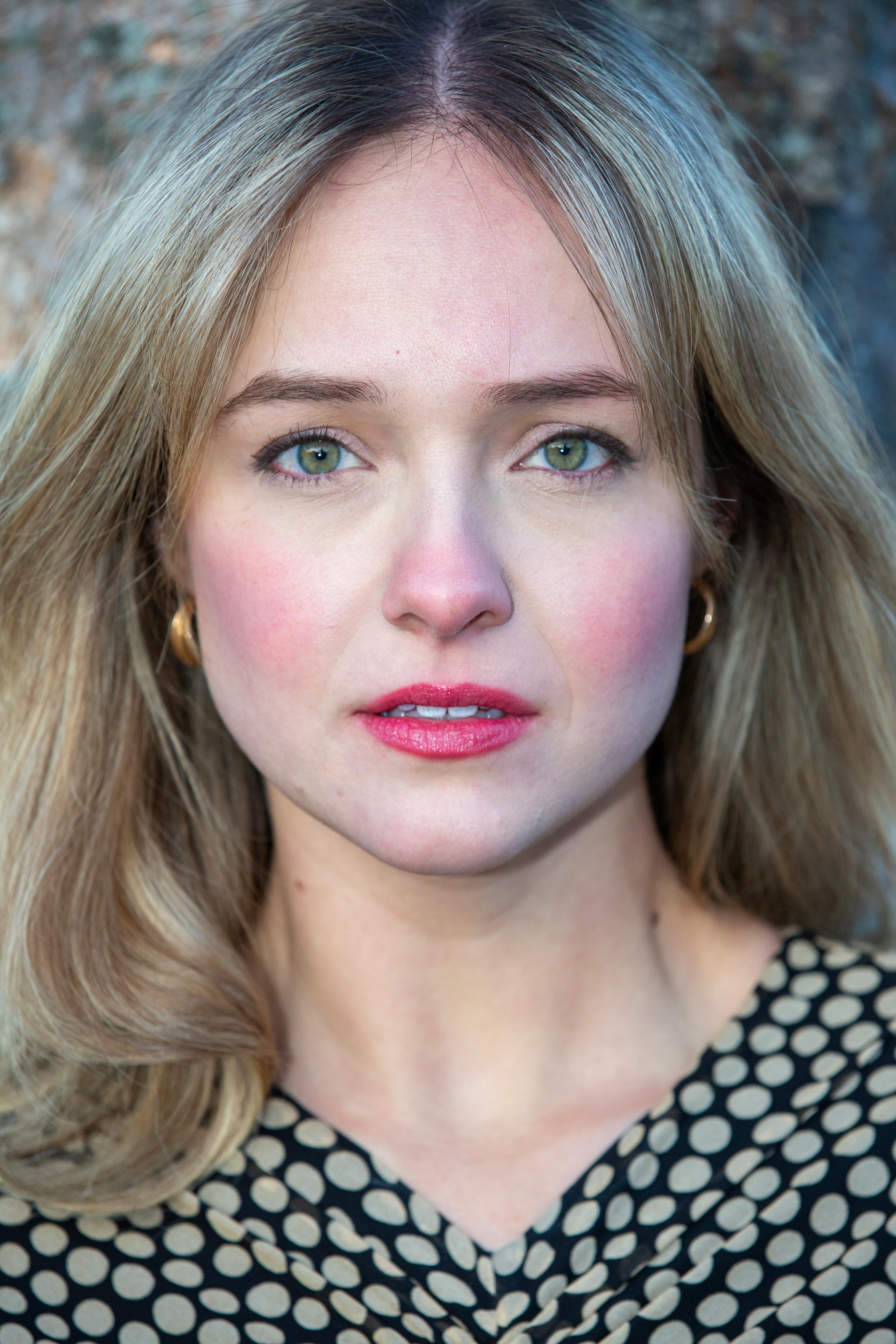 Detailed portrait of a blonde woman with green eyes against a blurred background.