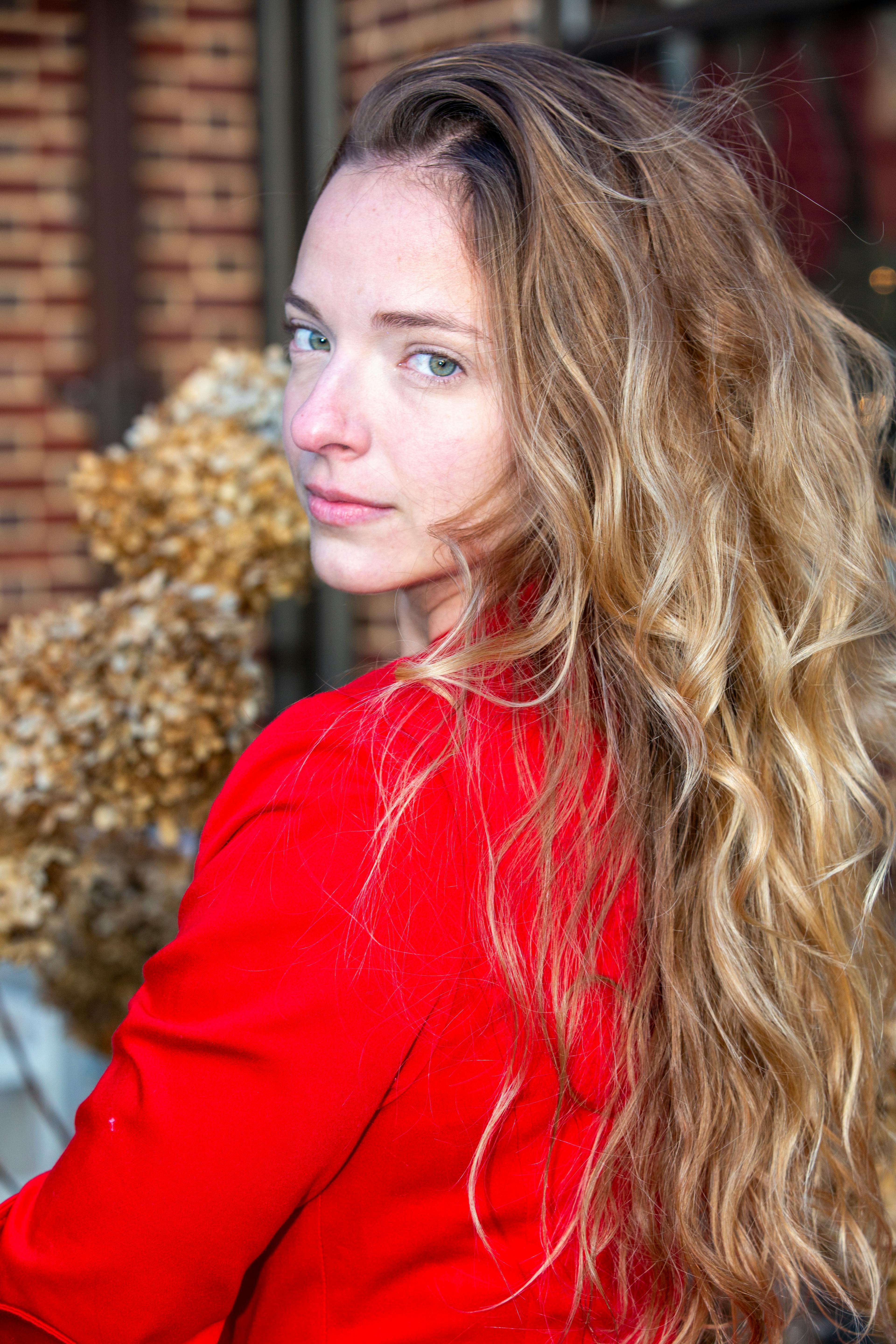 Outdoor portrait of a woman in red with long wavy hair, looking back.