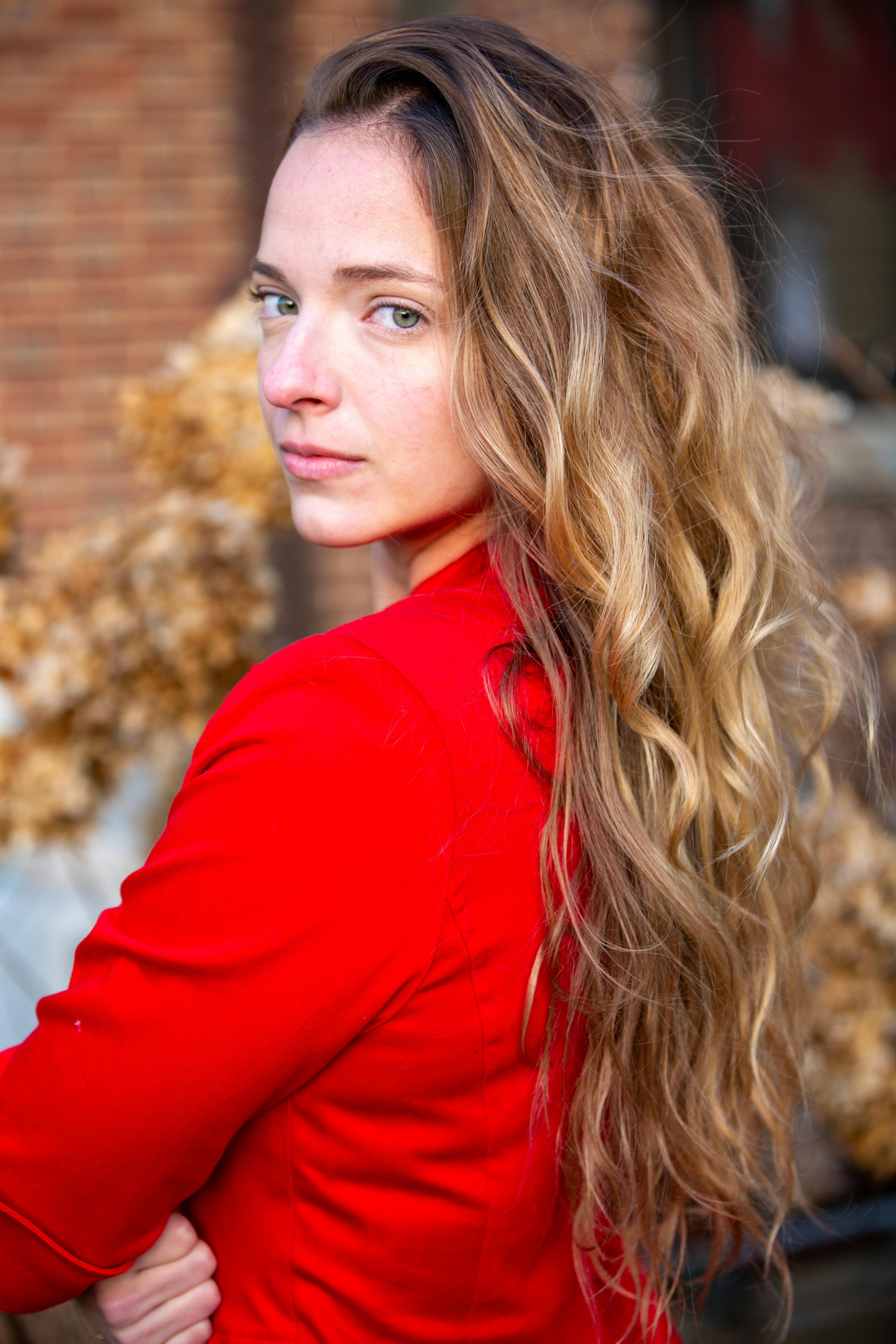 A captivating outdoor portrait of a woman in a red jacket showcasing long wavy hair.