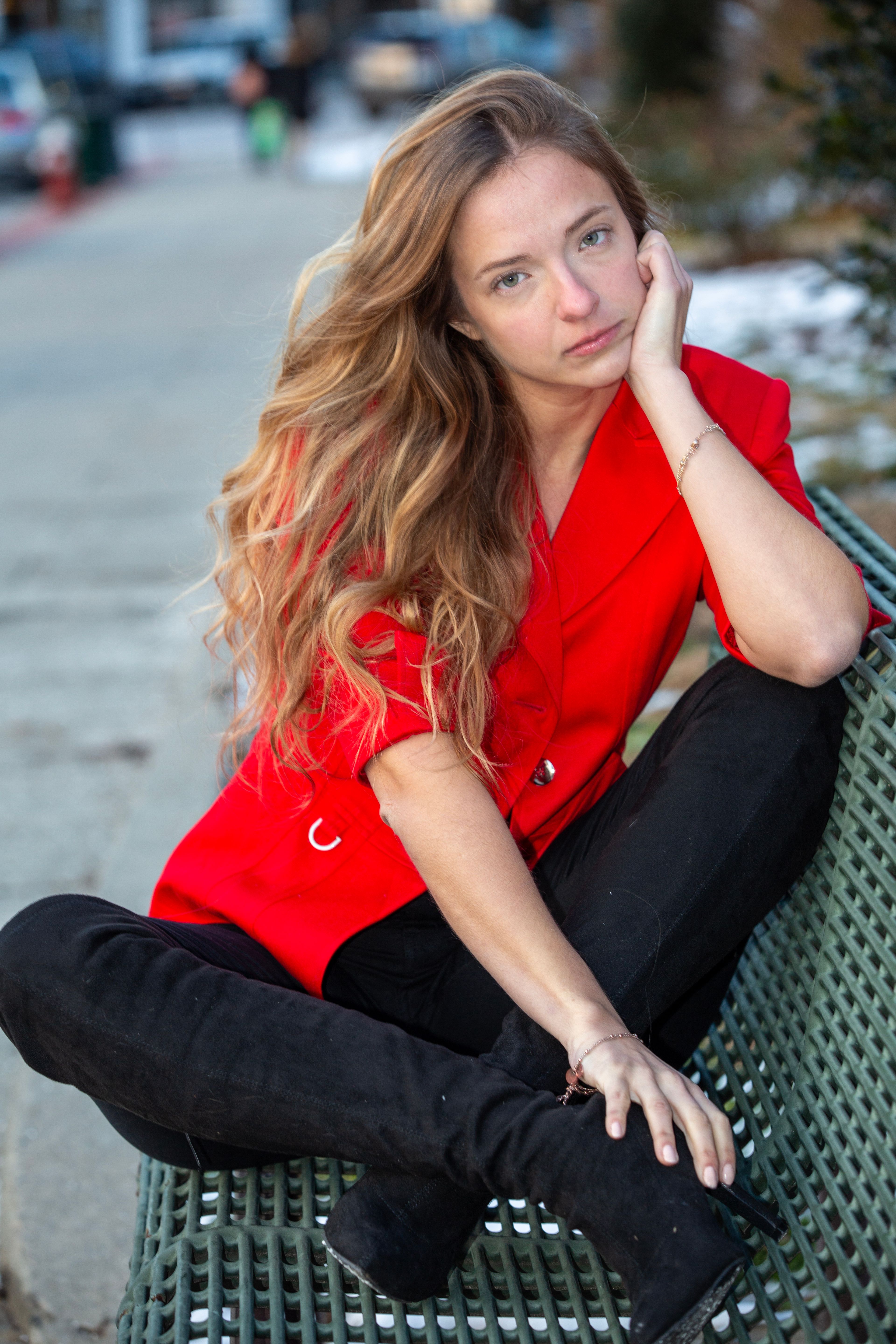 Portrait of a thoughtful young woman in a vibrant red jacket sitting on a bench outdoors.