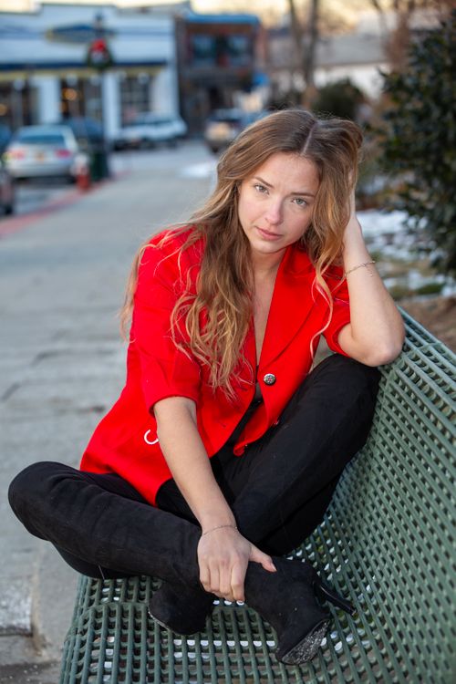 Free Young woman in a red jacket sitting on a city bench, urban setting. Stock Photo