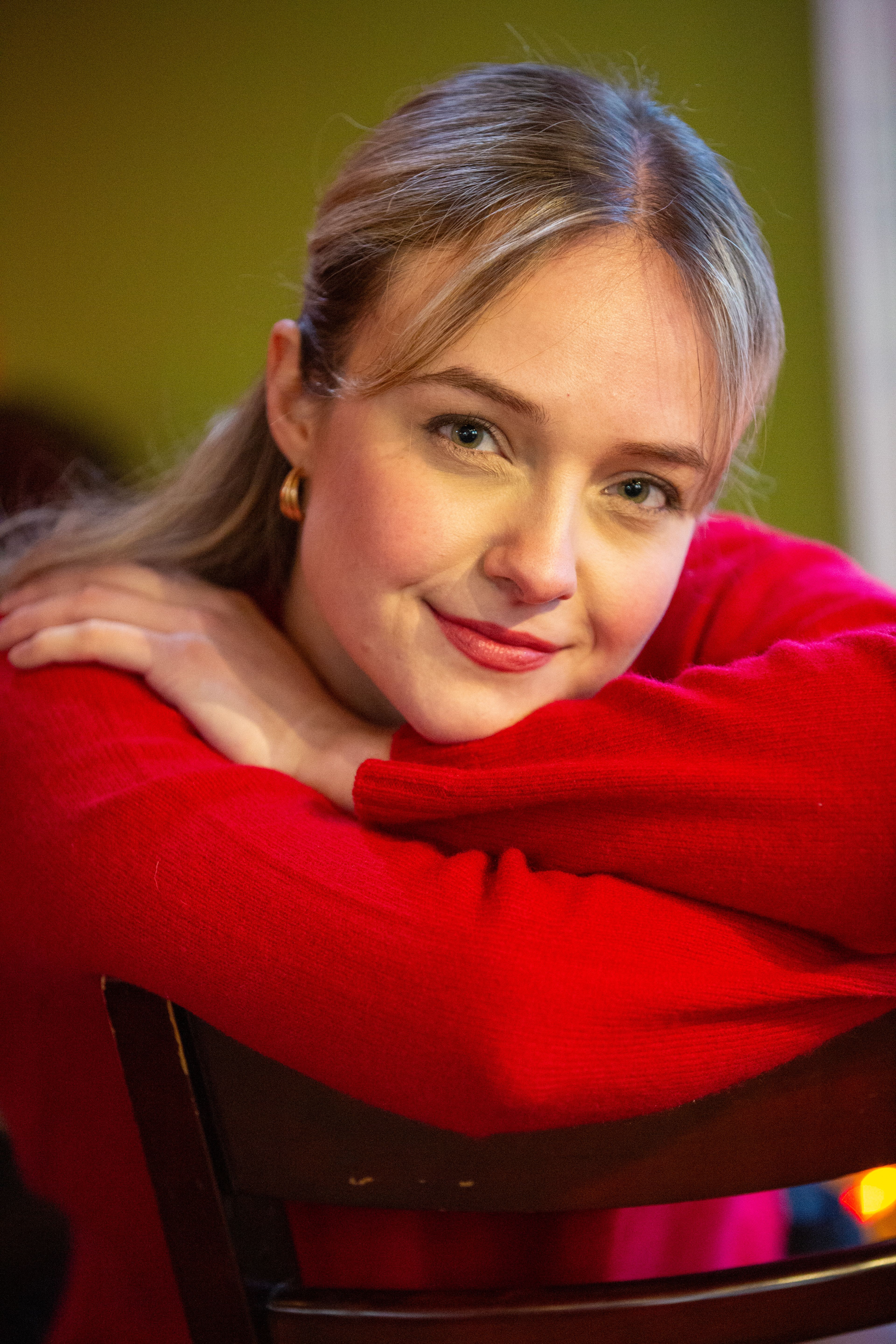 Smiling young woman in a red sweater relaxing indoors, showcasing a cheerful demeanor.