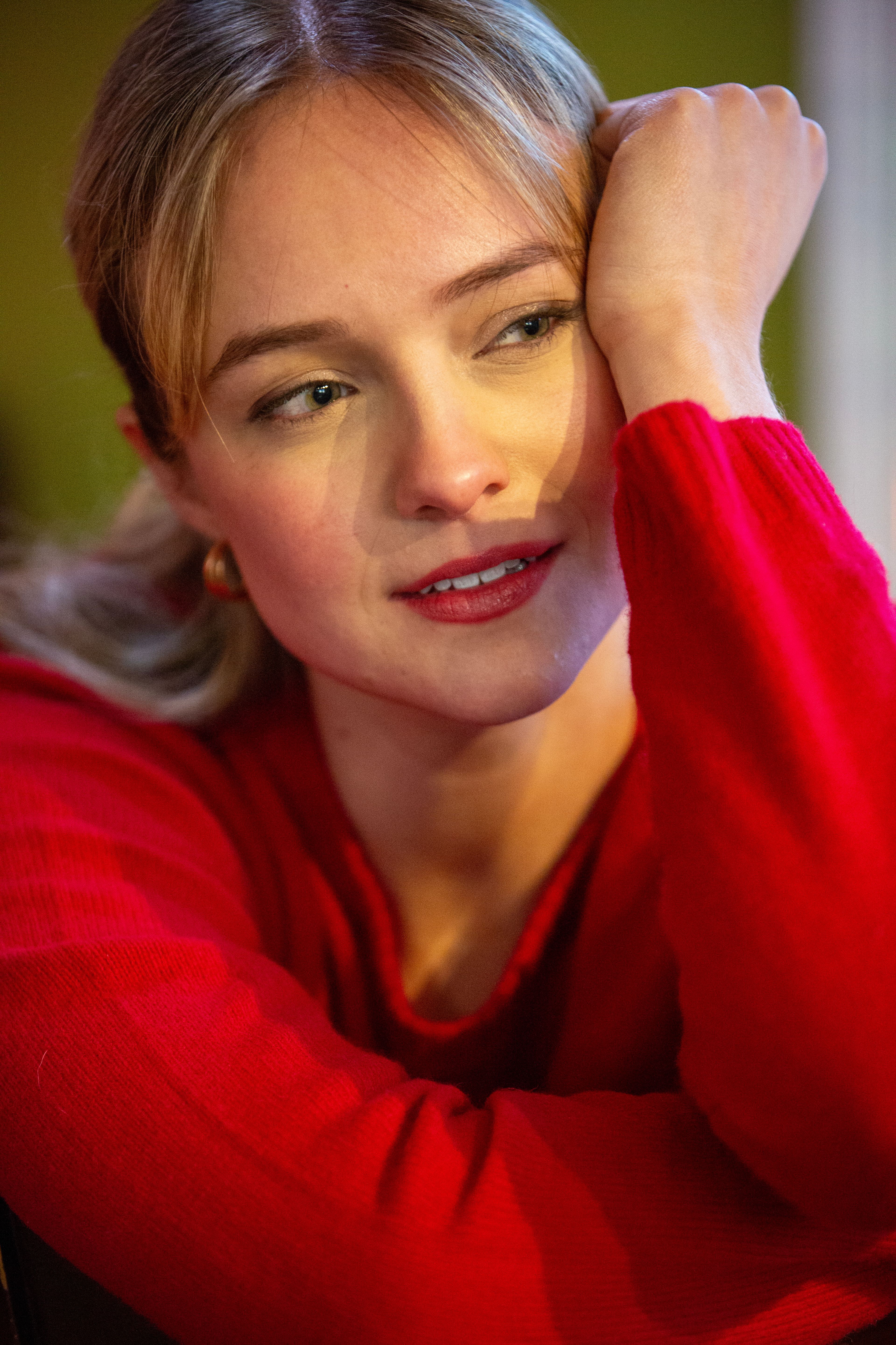 Close-up portrait of a woman in red, gazing thoughtfully indoors.
