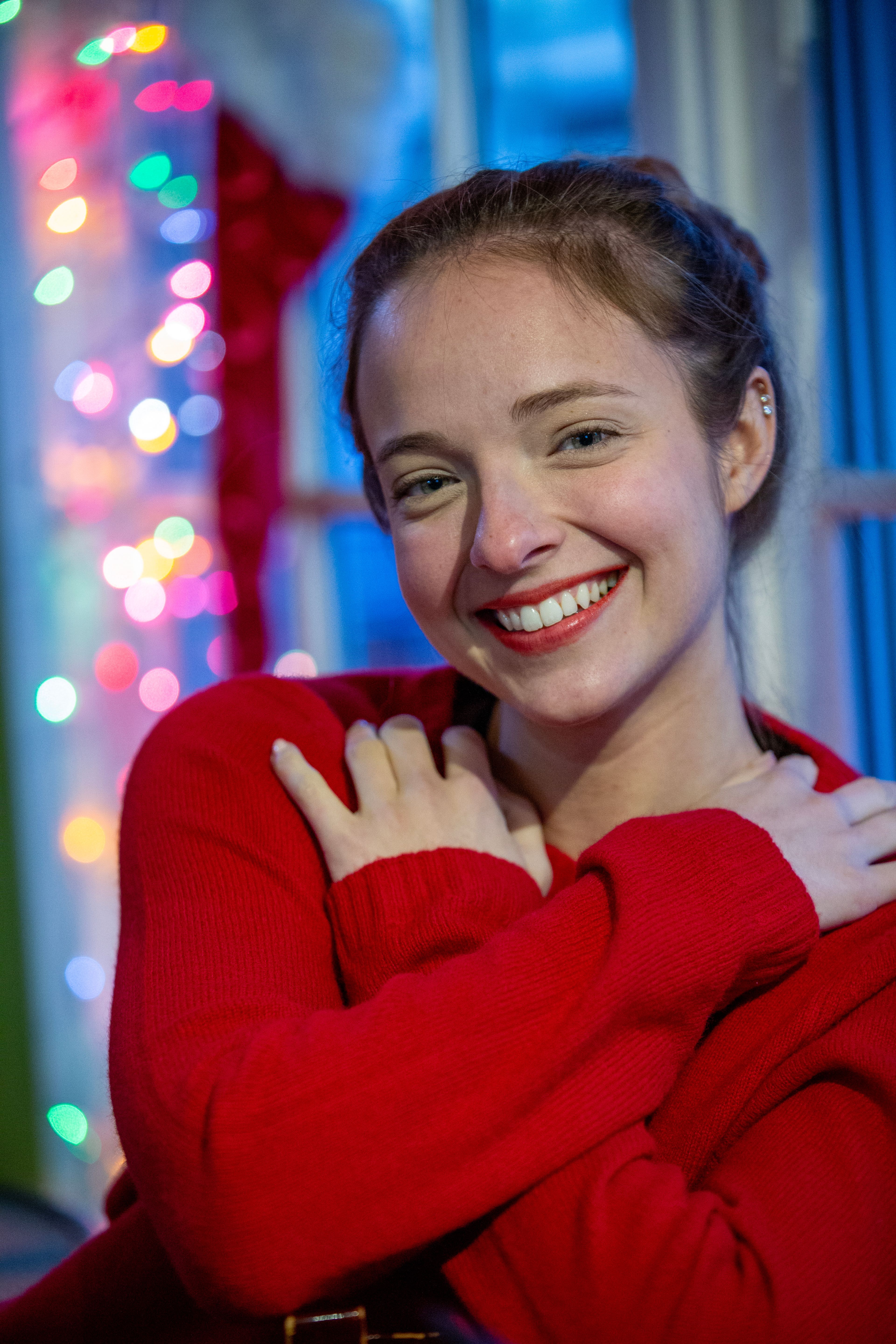 Smiling woman in red sweater with colorful bokeh lights indoors.