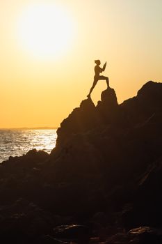 Dramatic silhouette of a person climbing rocks by the ocean at golden sunset.