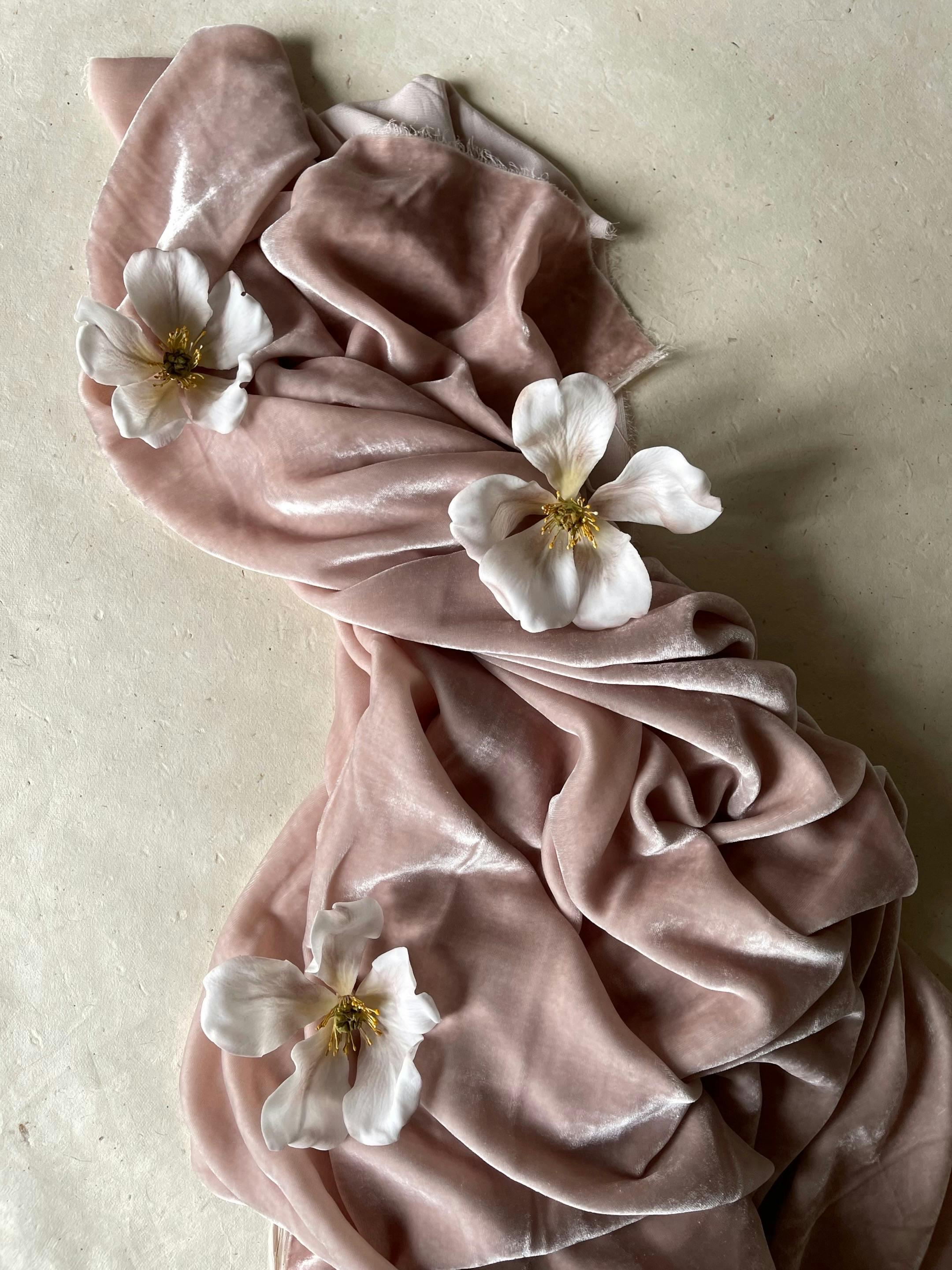 Soft pink velvet fabric with delicate white flowers in an artistic arrangement.