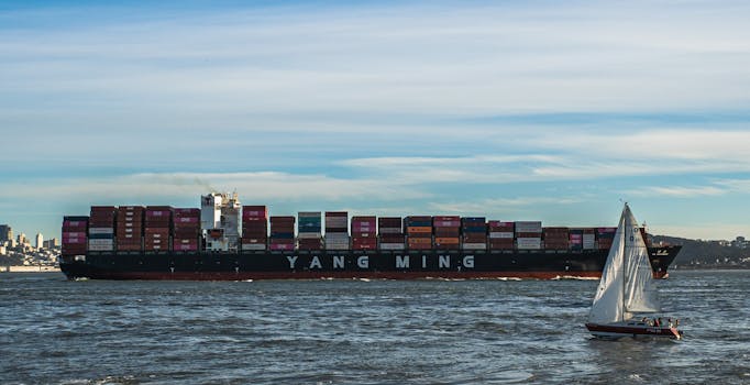 Container ship and sailboat navigating calm waters under a clear sky.