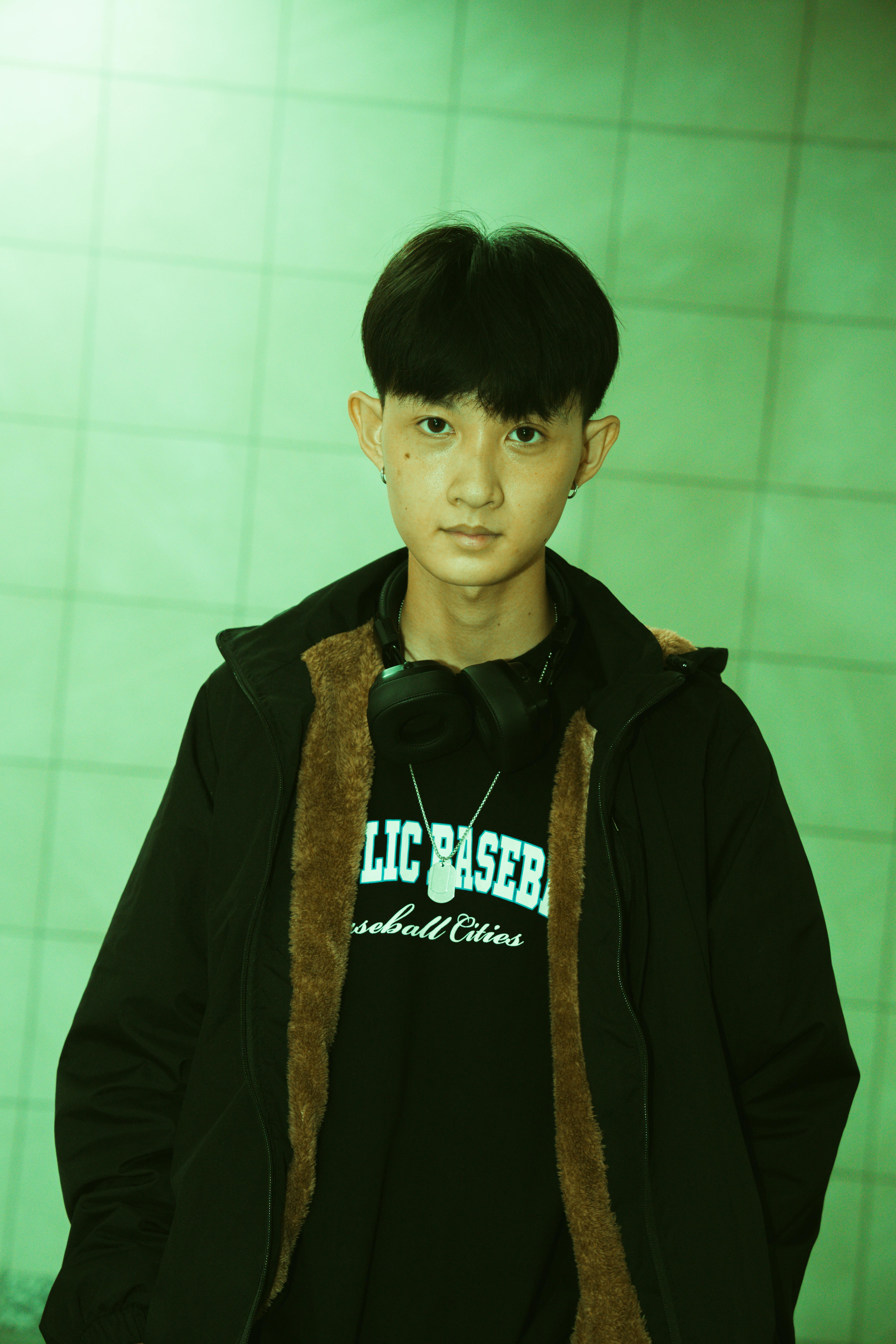 Portrait of a young male in urban fashion against a tiled wall, with green lighting effect.