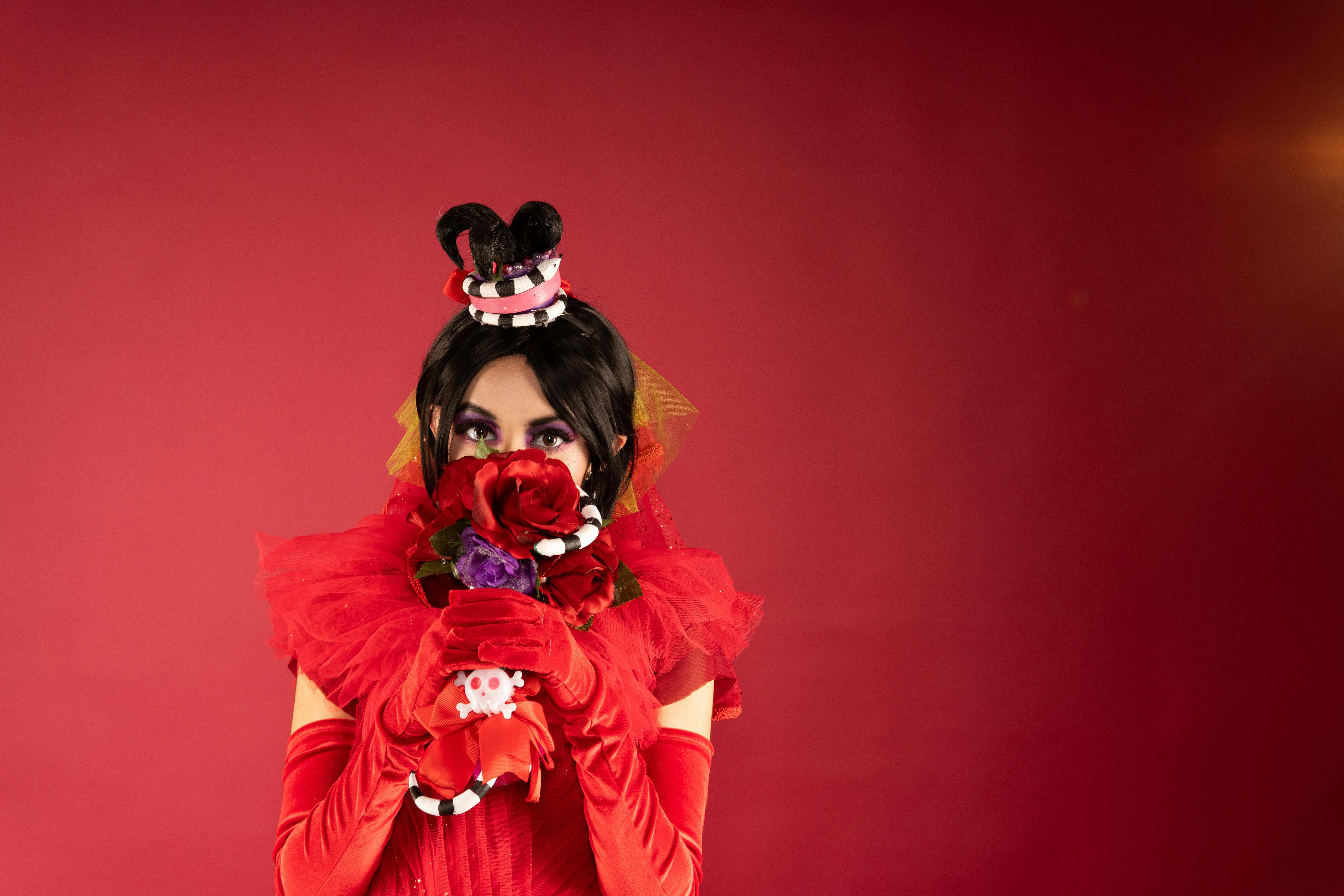 Ücretsiz Kırmızı kostümlü, siyah peruklu ve kırmızı güller tutan bir karakterin yer aldığı renkli cosplay portresi. Stok Fotoğraflar