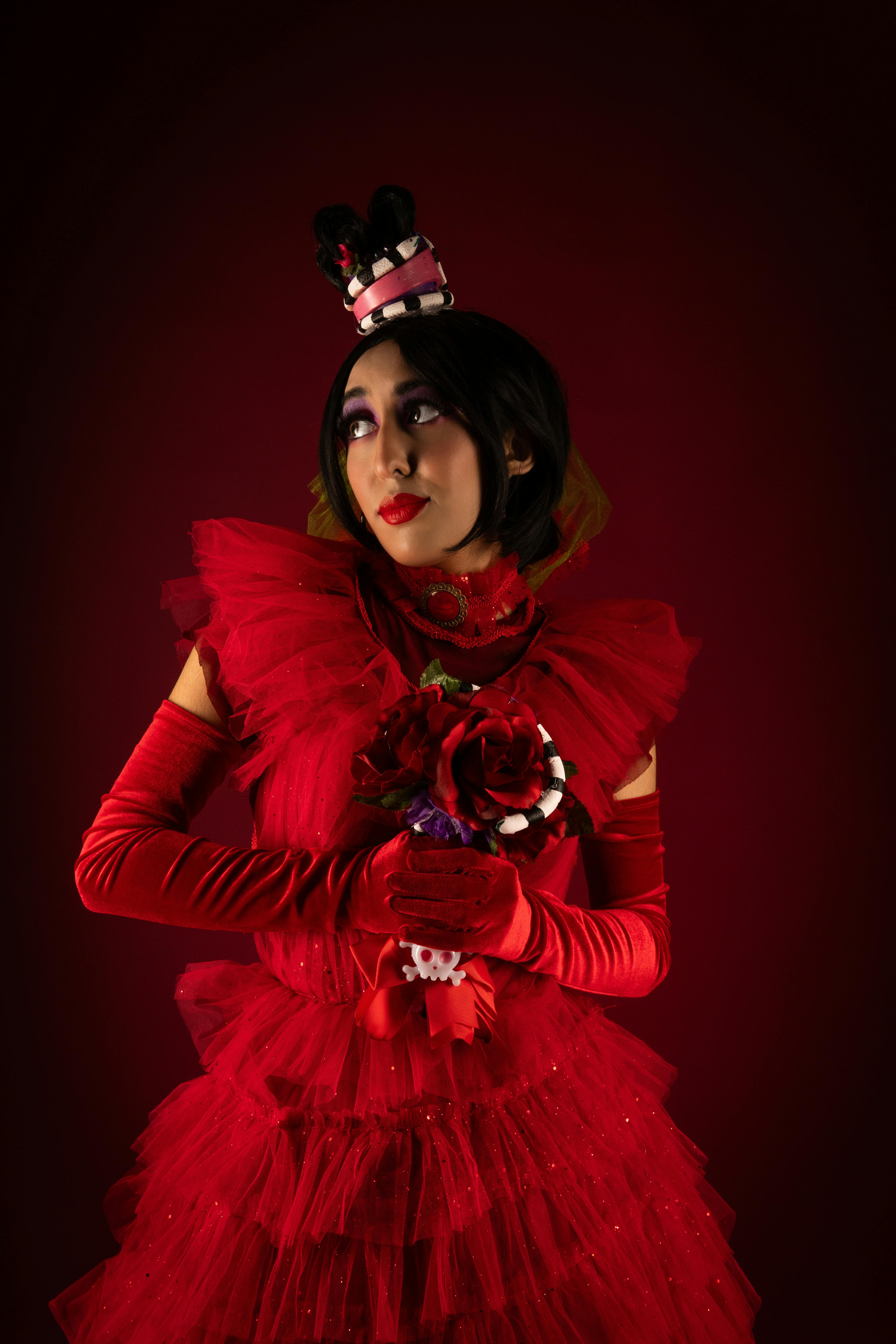 Creative portrait of a person in elaborate red costume with a whimsical hat, set against a red background.
