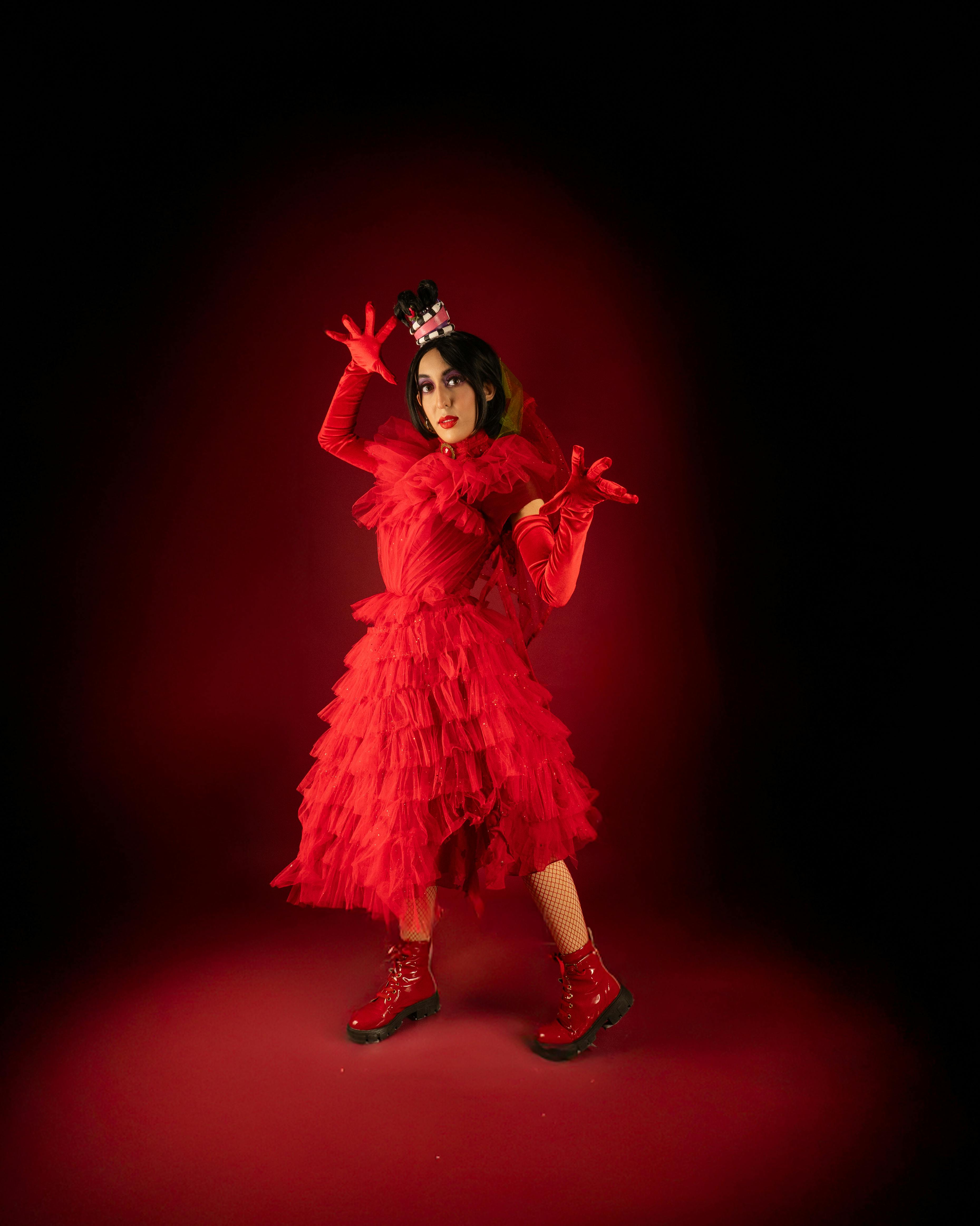 Ücretsiz Kırmızı bir arka plan önünde kırmızı kostüm ve siyah peruk giyen bir kişinin yer aldığı büyüleyici bir cosplay fotoğrafı. Stok Fotoğraflar