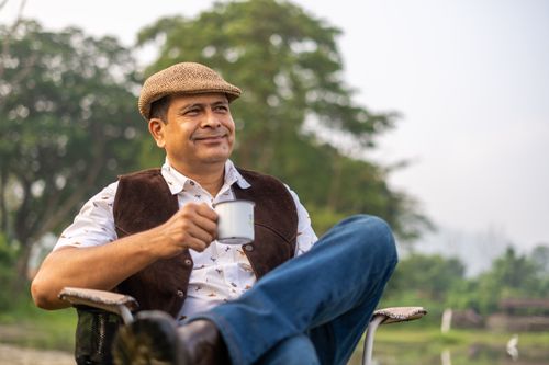 Free A man enjoys a relaxing moment outdoors with a cup of coffee surrounded by nature. Stock Photo