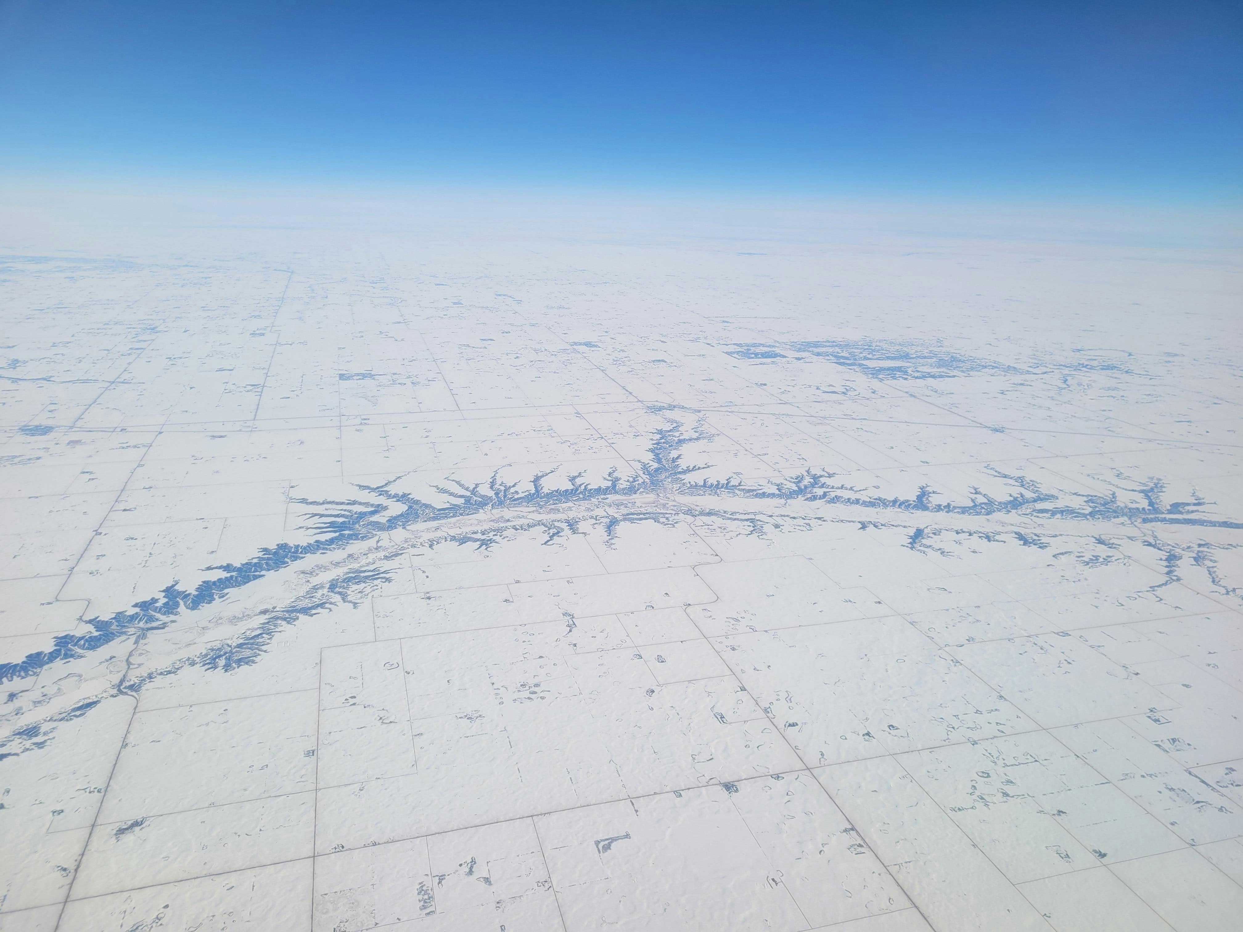 A breathtaking aerial shot showcasing a vast snow-covered landscape under a clear blue sky during winter.