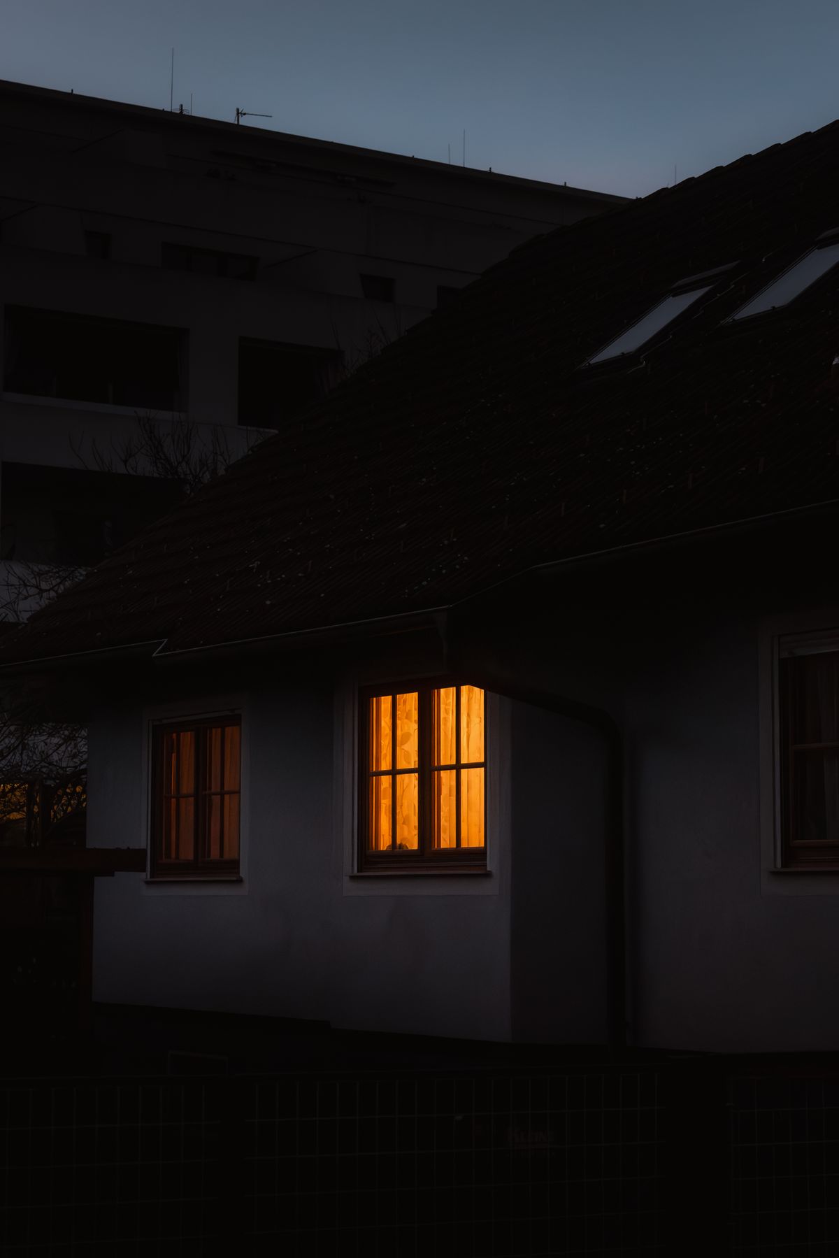 Meleg fény szűrődik ki egy ház ablakán alkonyatkor