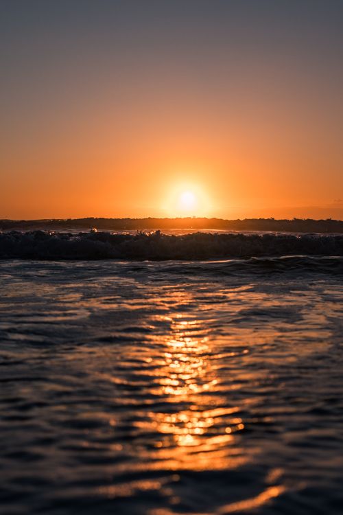 Free Peaceful sunset casting warm hues over ocean waves with a soft, tranquil glow. Stock Photo