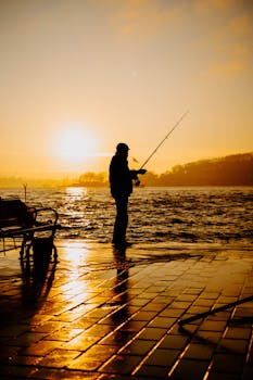 Silhouette of a fisherman casting at sunset with vibrant reflections on the water.