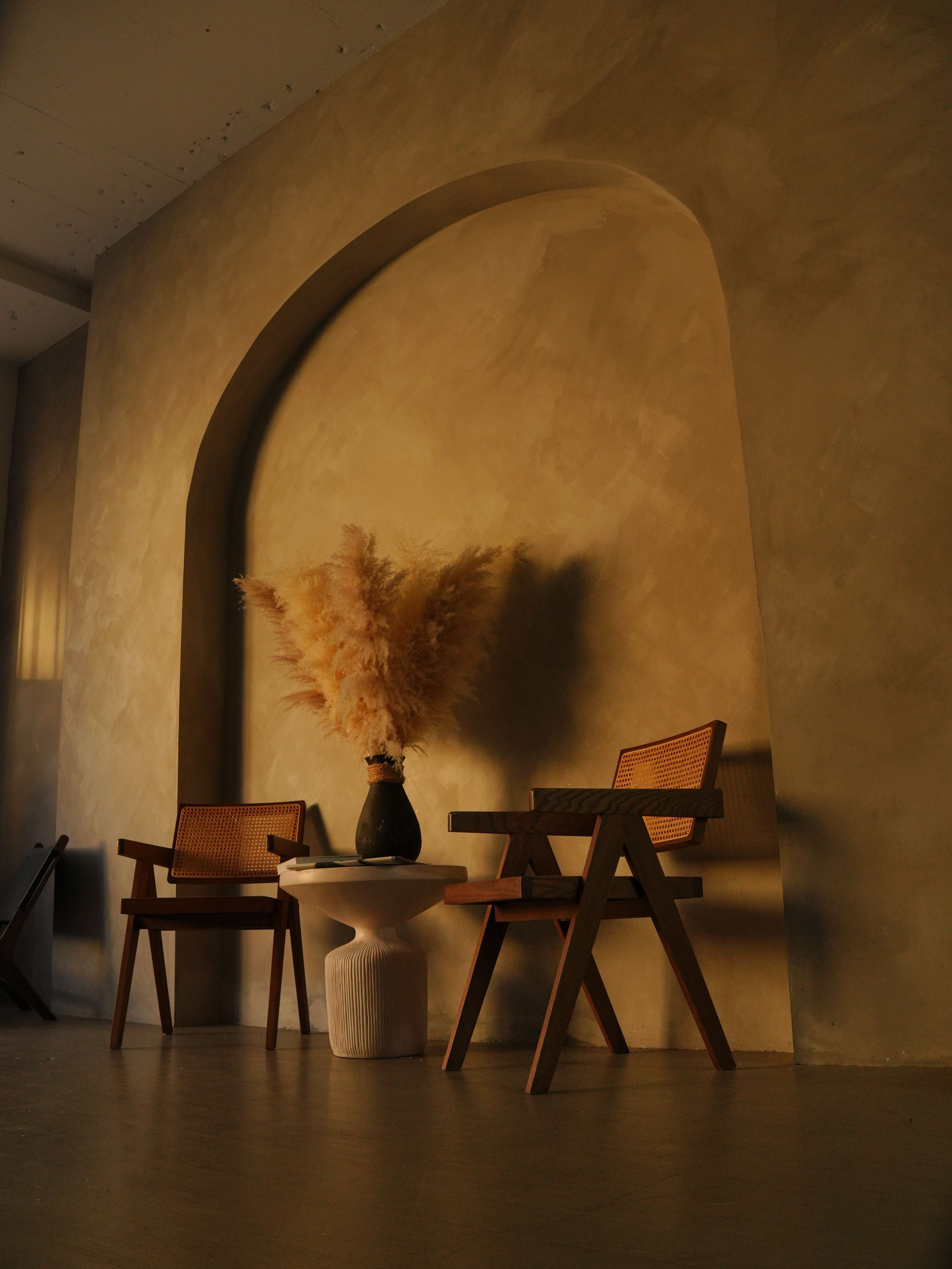 Warm and cozy interior scene featuring rattan chairs, pampas grass, and a side table.
