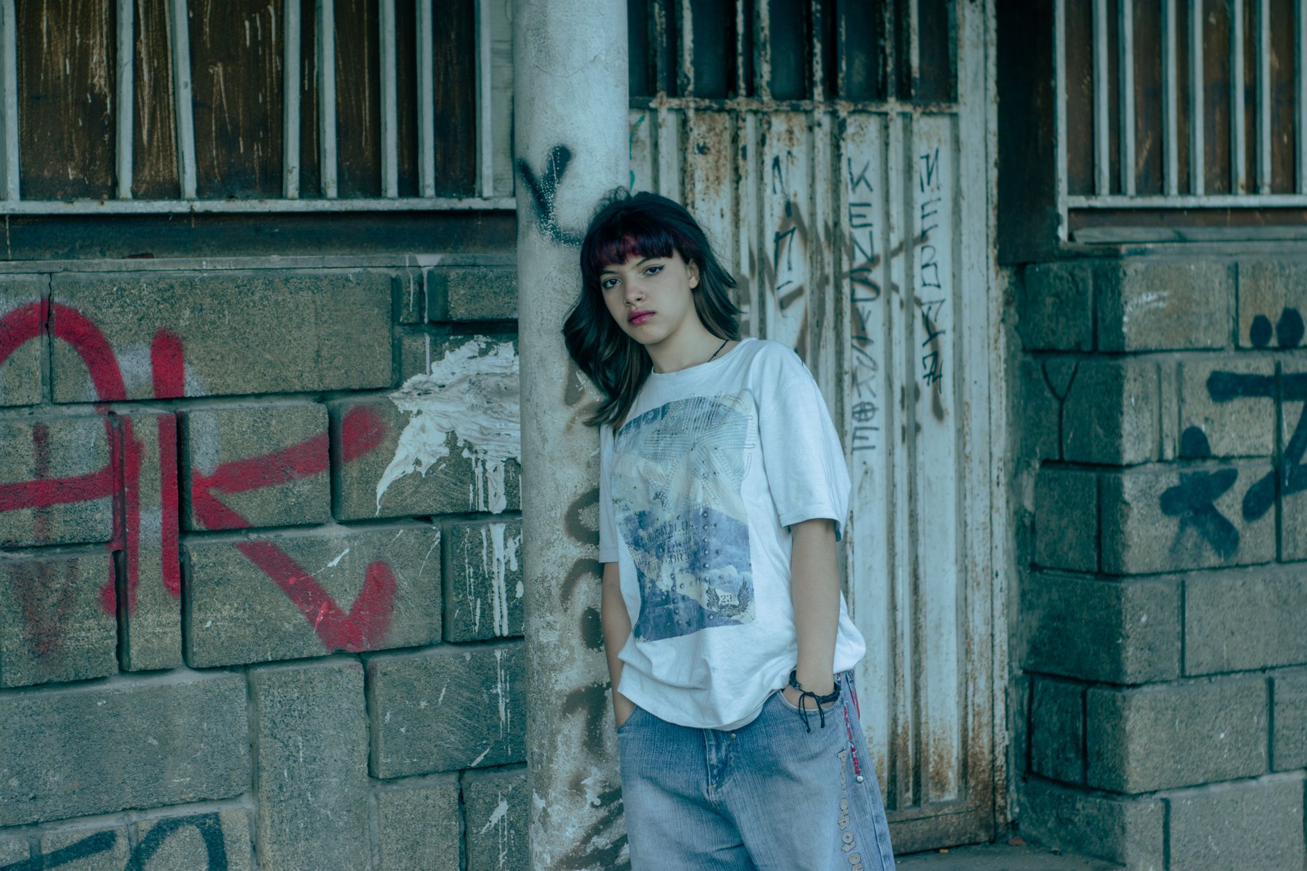 Jeune femme en tee-shirt oversize graphique et jean ample dans une ruelle taguee, look streetwear feminin