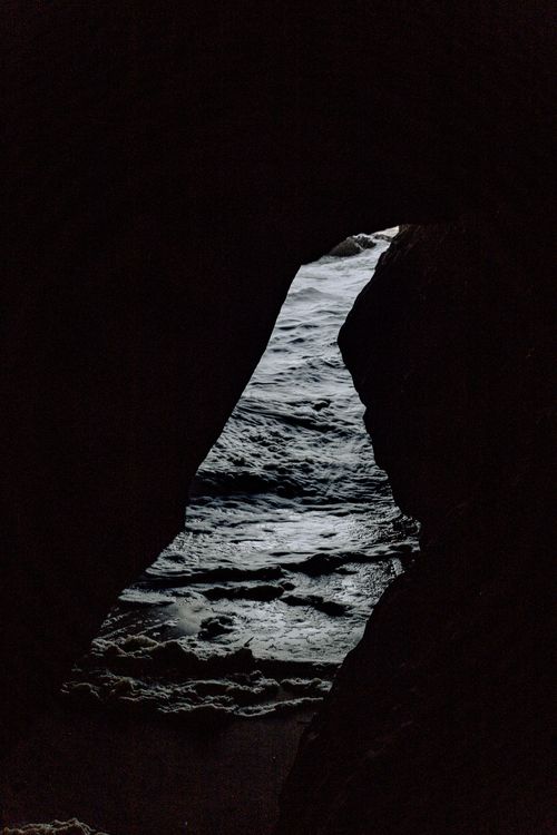 Free A captivating glimpse of the ocean waves through a rugged sea cave's natural opening. Stock Photo