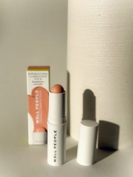 Natural peach cream blush in stick form displayed with packaging. Minimalist style.